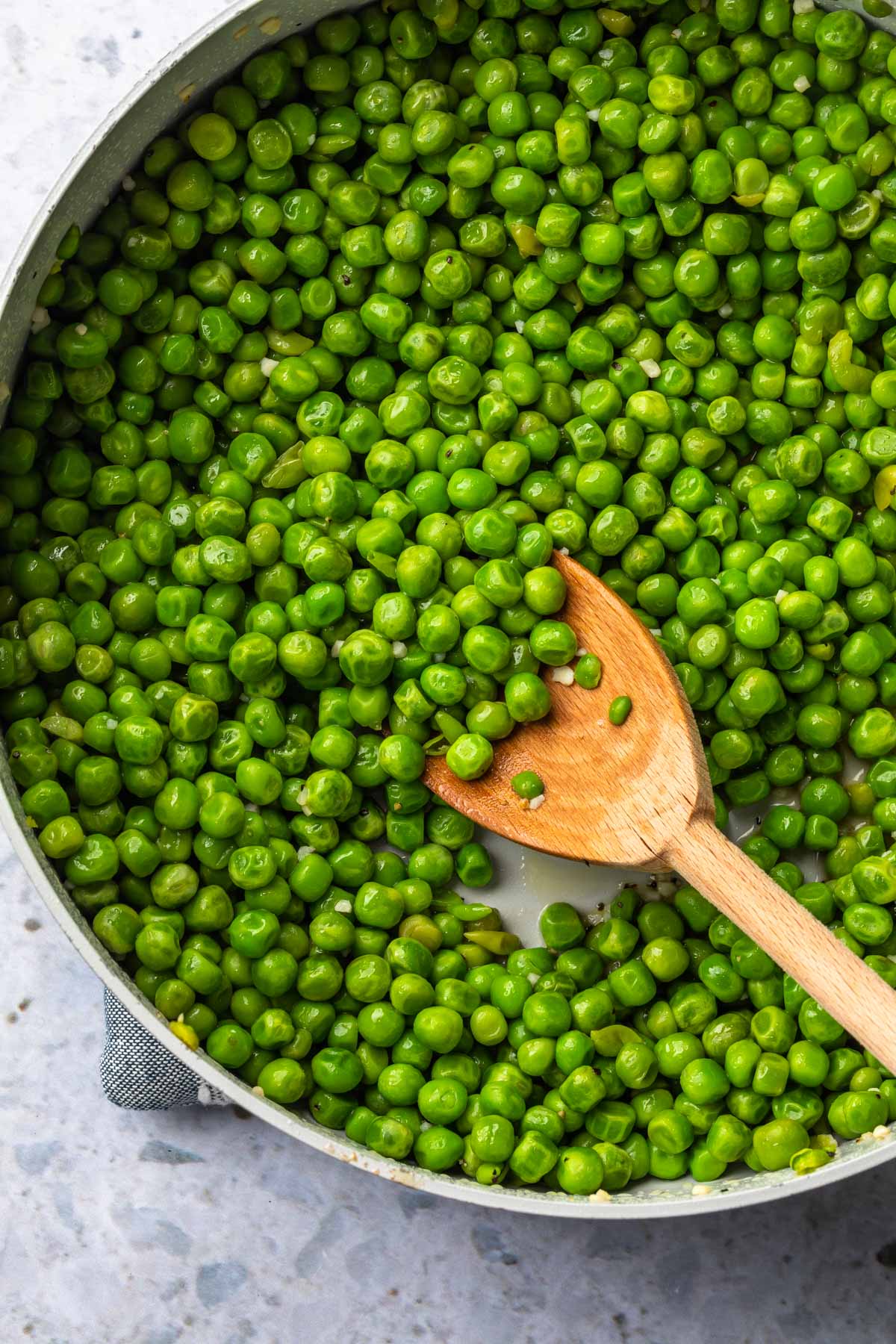 Close up of peas in a skillet being stirred with a wooden spoon. 