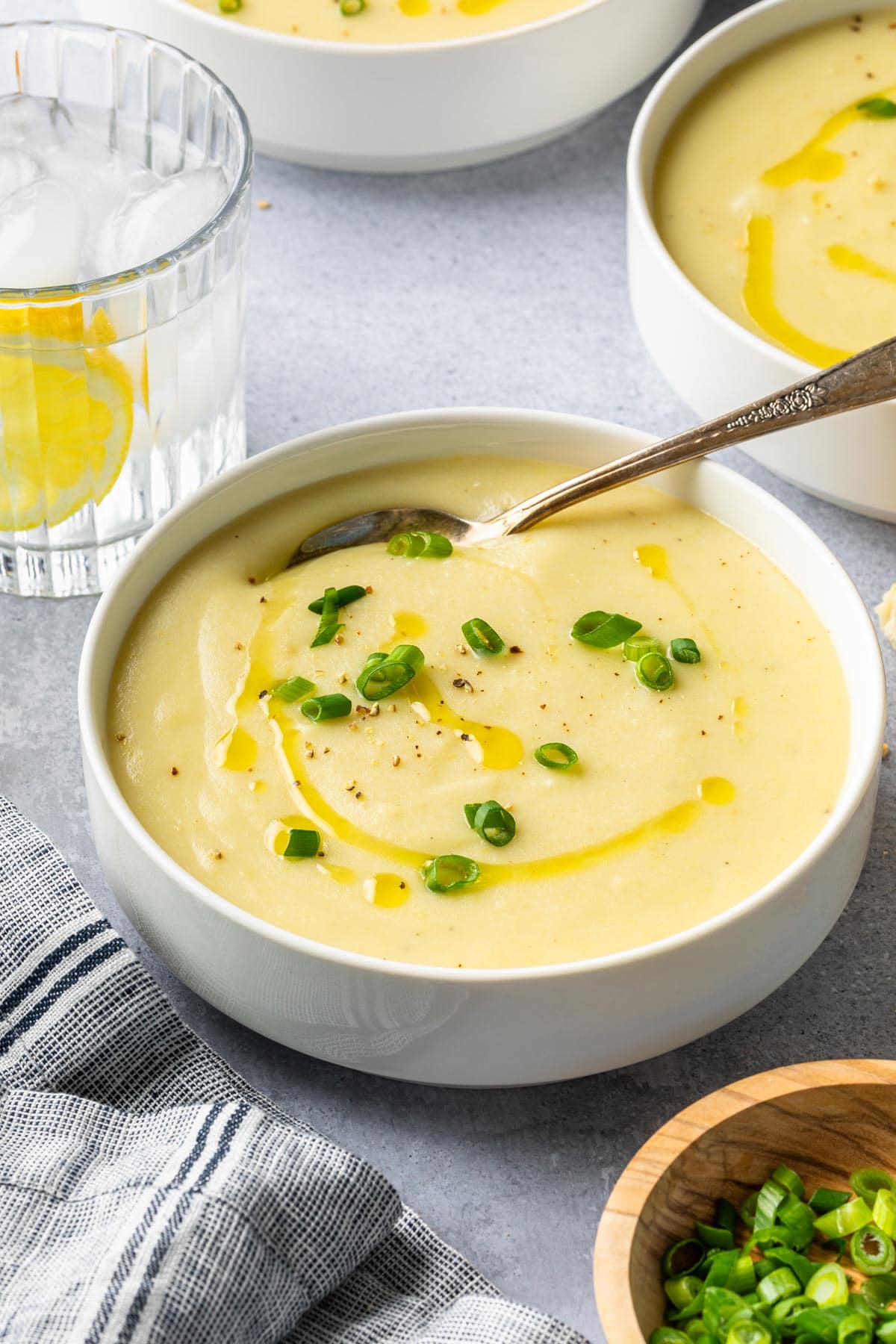 a few bowls of potato soup with a glass of lemon water next to them. 