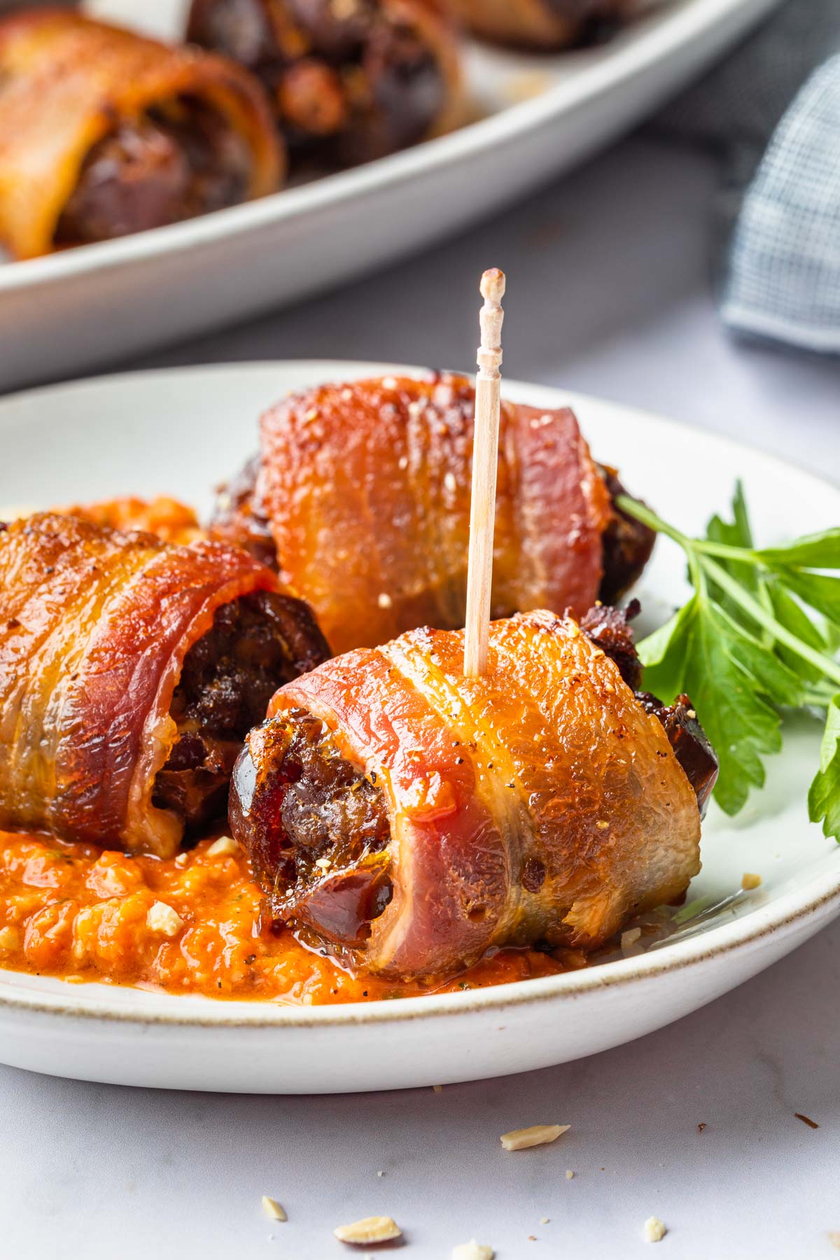 Close up of bacon wrapped dates on a plate with a toothpick in one. 