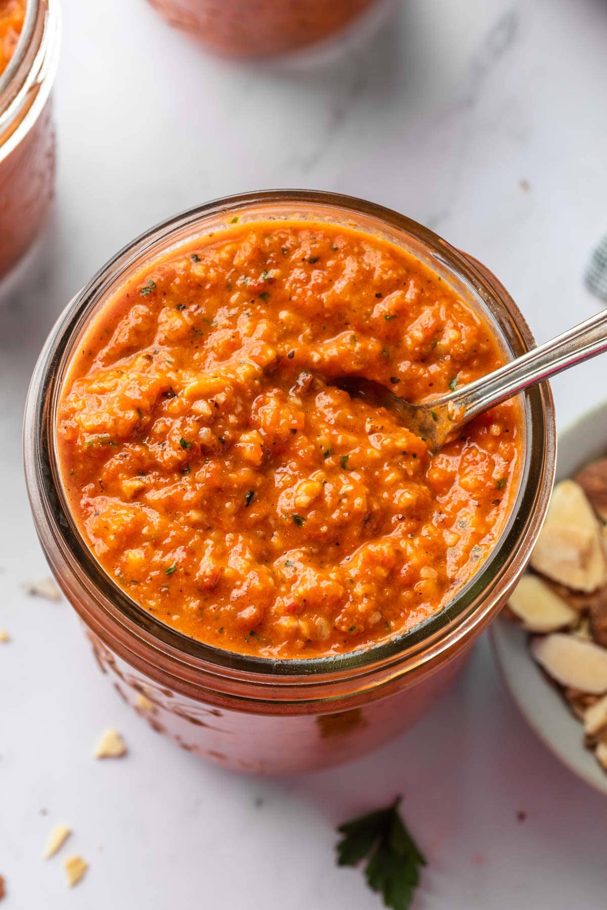 An overhead close up shot of romesco sauce in a mason jar with a spoon in it. 