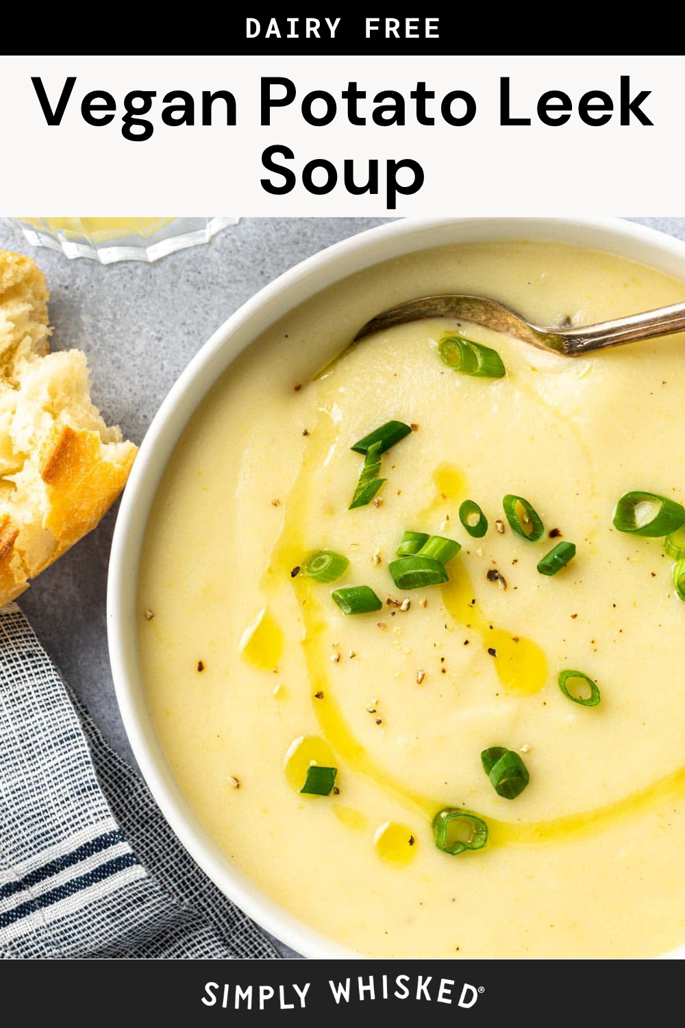 Bowl of creamy Vegan Potato Leek Soup topped with sliced green onions and drizzled with olive oil, with a spoon in the bowl and a piece of bread on the side.