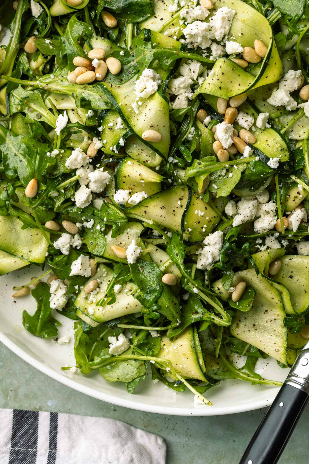 Close up of zucchini salad topped with dairy free feta crumbles and pine nuts. 
