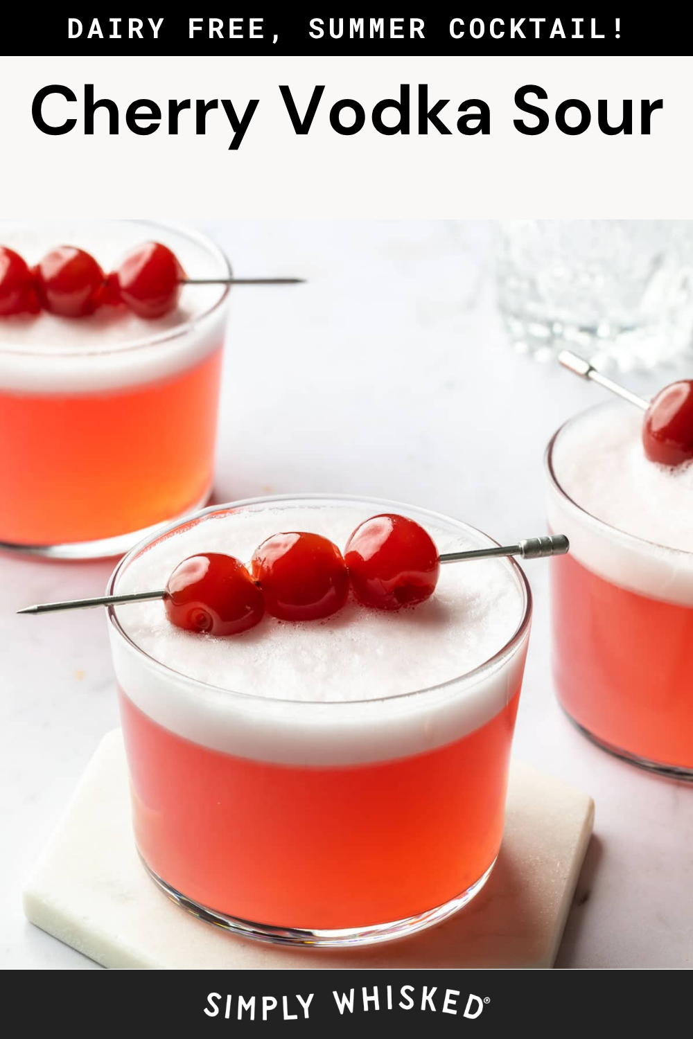 Three glasses of cherry vodka sour cocktails with frothy tops, each garnished with three cherries on a cocktail pick. The text above reads “Cherry Vodka Sour,” perfectly capturing the vibrant, inviting look of this classic cherry vodka sour drink, and below, “Simply Whisked.”.