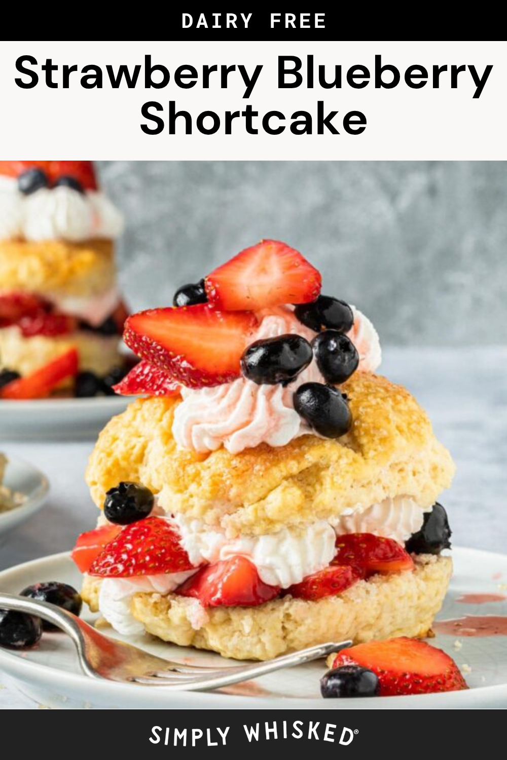 A Strawberry Blueberry Shortcake sits on a white plate, featuring a dairy-free shortcake topped with whipped cream, strawberries, and blueberries, while another shortcake rests in the background.