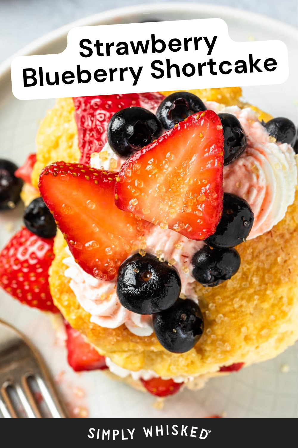 A close-up of Strawberry Blueberry Shortcake topped with whipped cream, fresh strawberry slices, blueberries, and sprinkled sugar. A fork is visible on the plate. Text reads “Strawberry Blueberry Shortcake” and “Simply Whisked.”.