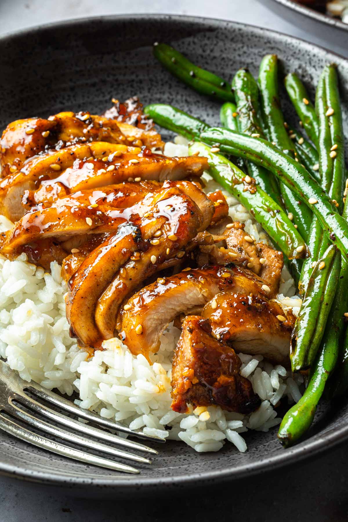 Close up of teriyaki chicken and green beans on a bowl of white rice. 