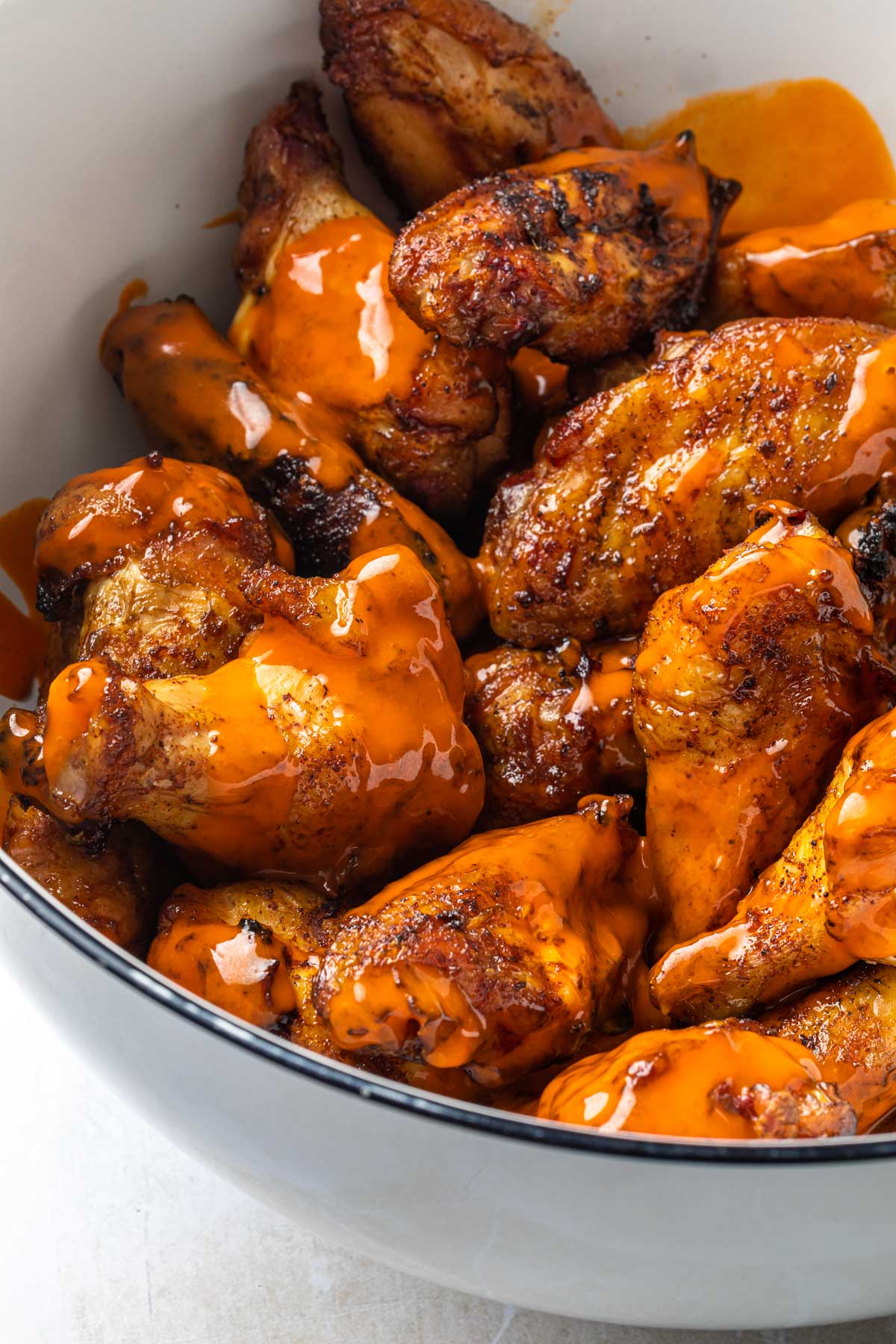 Smoked chicken wings in a bowl drizzled with buffalo sauce. 