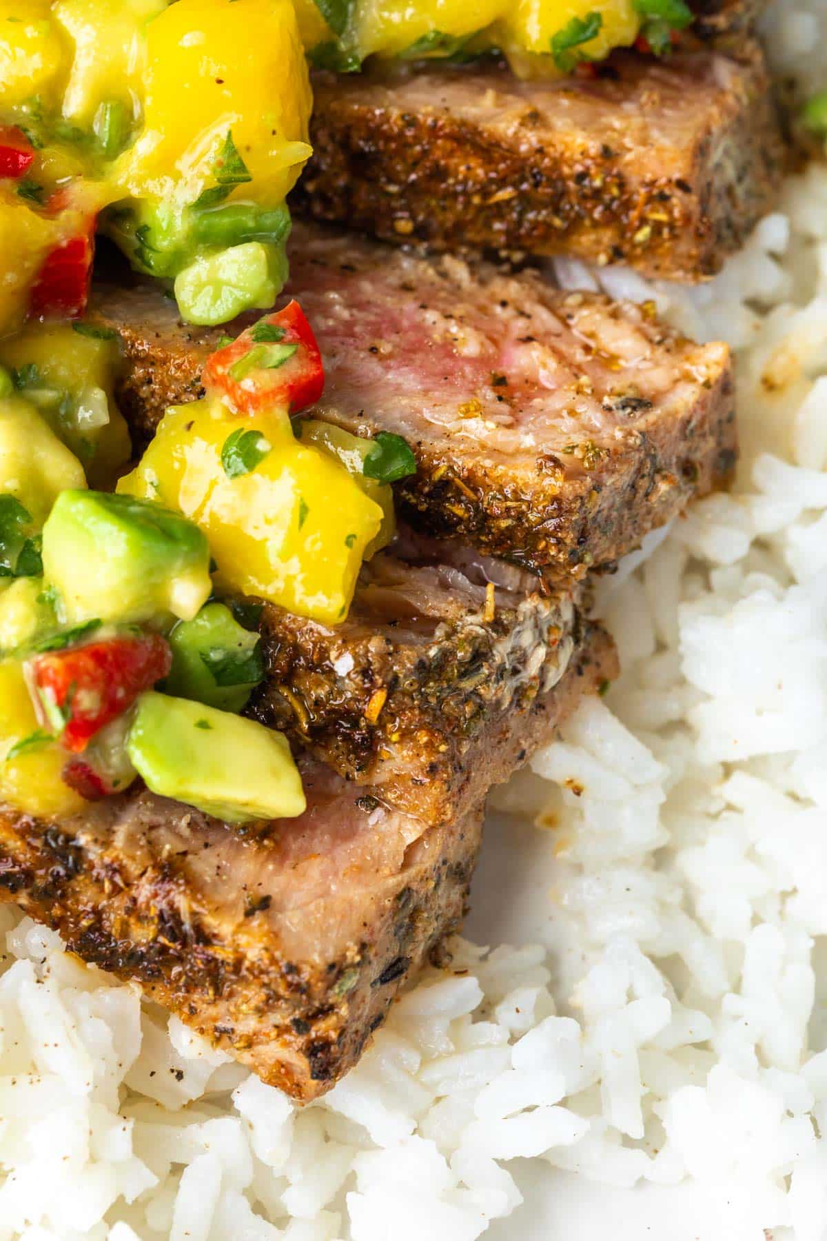 A close up of a blacked tuna steak sliced with mango avocado salsa on top of rice. 