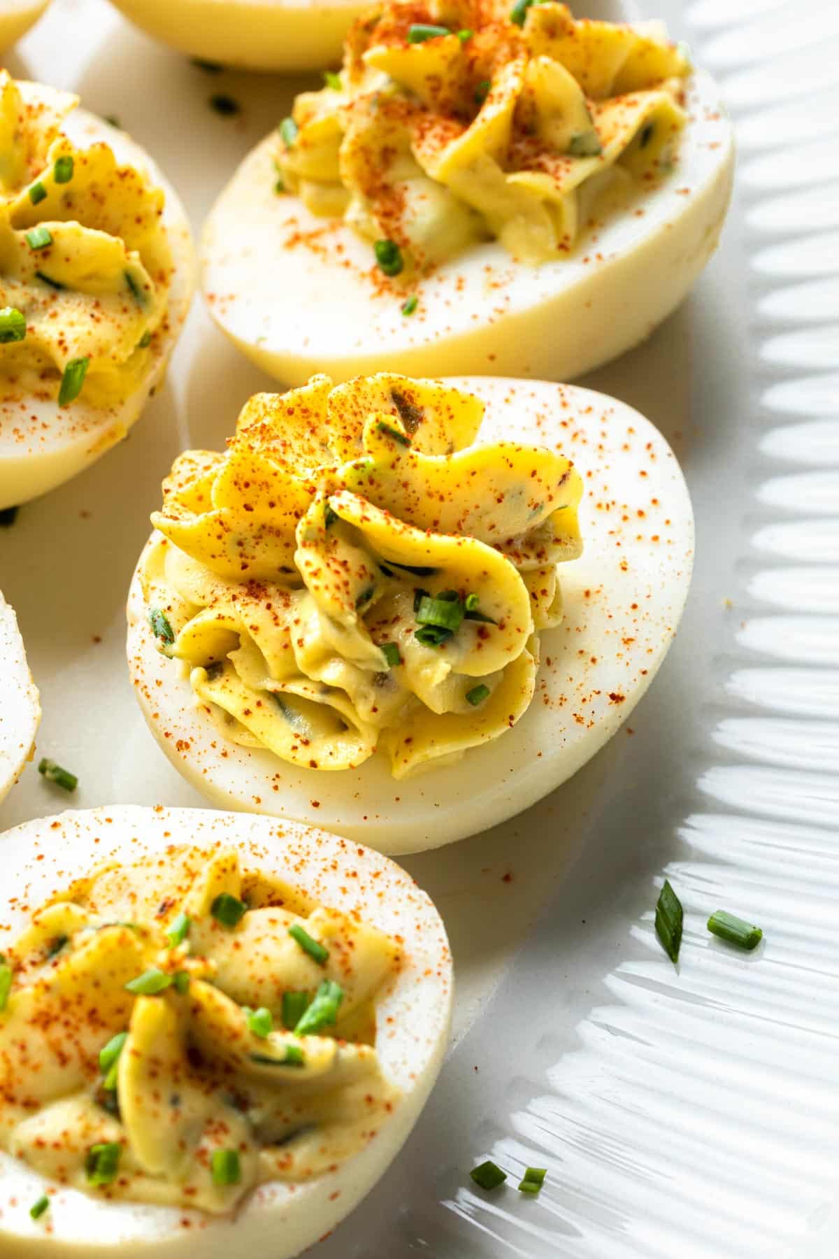 Close up of smoked deviled eggs on a platter, garnished with smoked paprika and chopped fresh chives. 