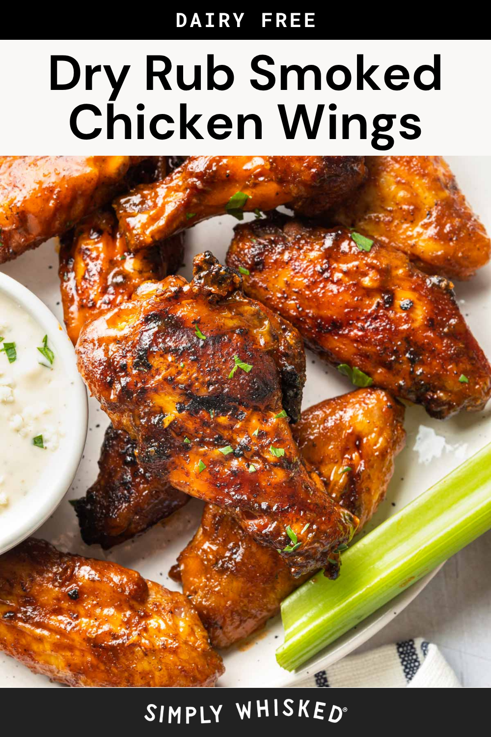 A plate of glazed smoked chicken wings garnished with herbs, served with celery sticks and a cup of dipping sauce on the side. Text reads: “Smoked Chicken Wings—Dairy Free Dry Rub. Simply Whisked.”.