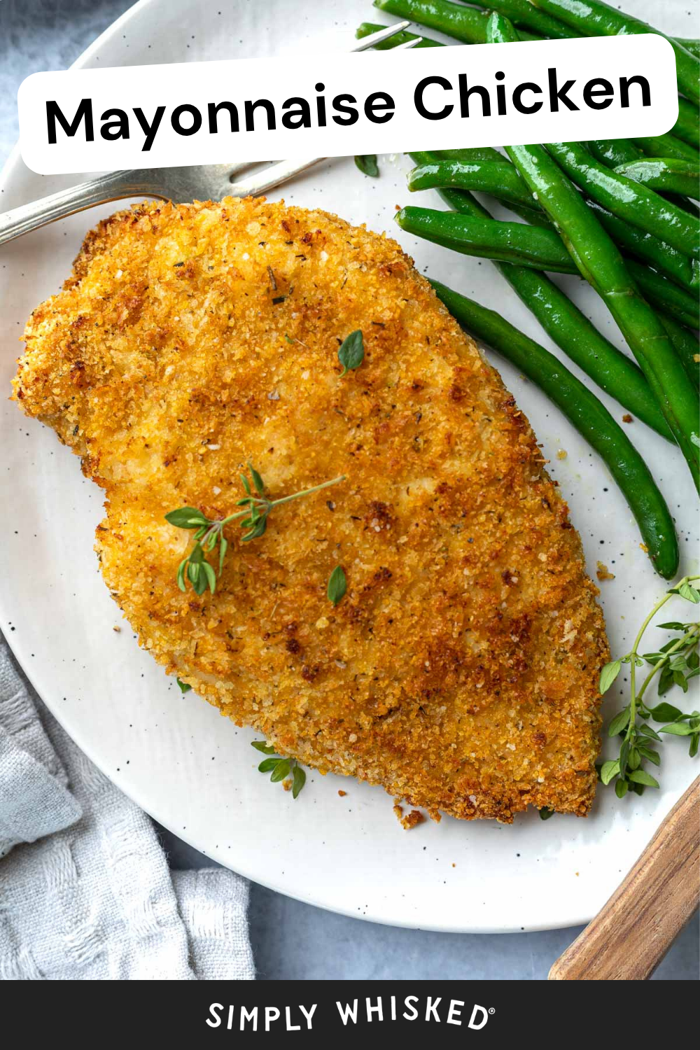 A breaded, baked Mayonnaise Chicken breast garnished with fresh herbs is served on a white plate with green beans. A fork and light gray napkin are placed beside the plate. Text reads Mayonnaise Chicken and Simply Whisked.