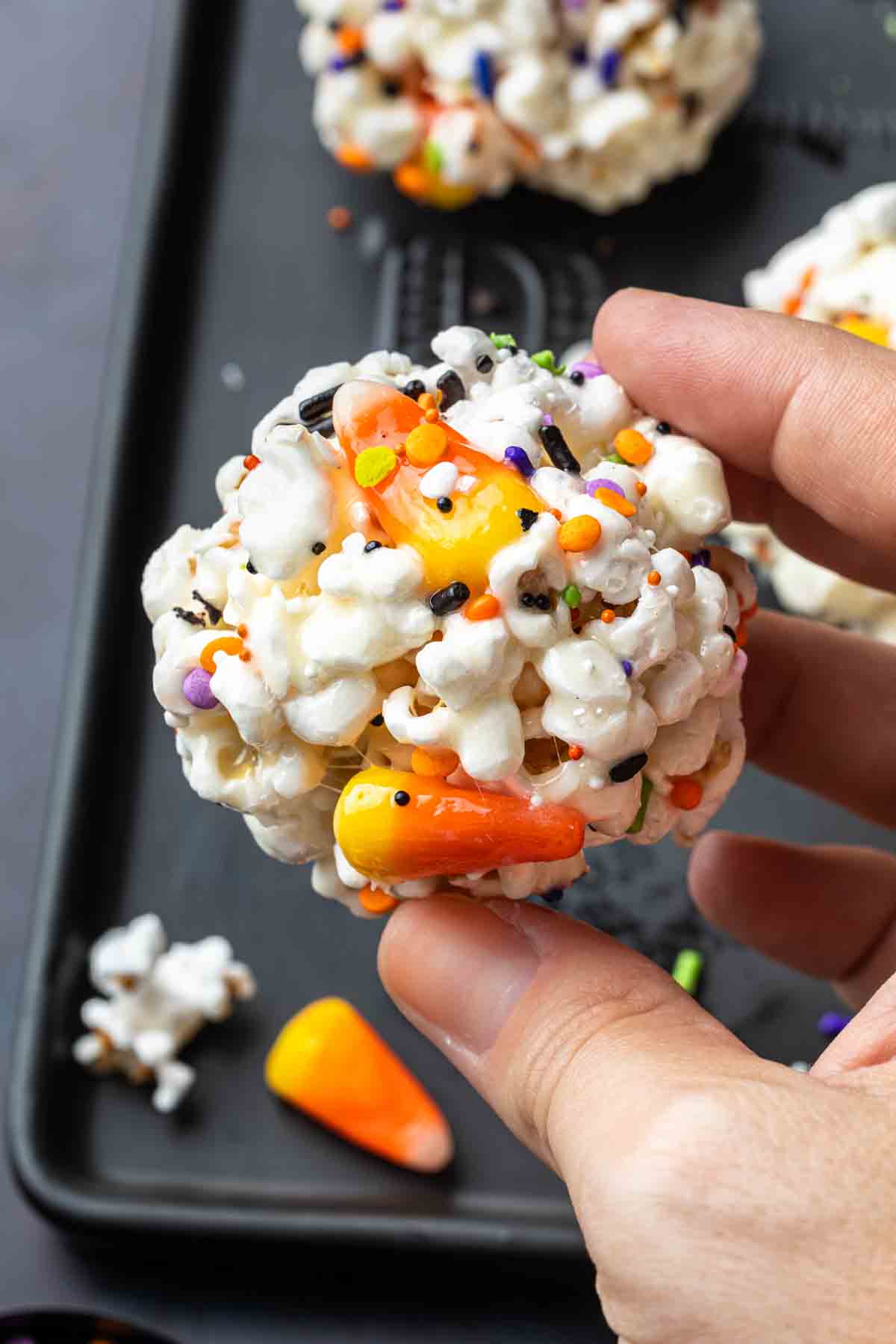 Close up of a halloween popcorn ball made with marshmallows, candy corn and halloween sprinkles. 
