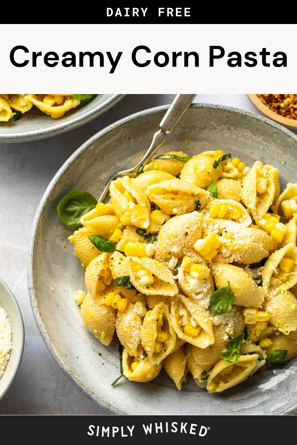 A bowl of shell corn pasta mixed with creamy corn sauce, garnished with herbs and dairy-free cheese, sits on a table with a fork and side dishes nearby. The text above reads Dairy Free Creamy Corn Pasta.