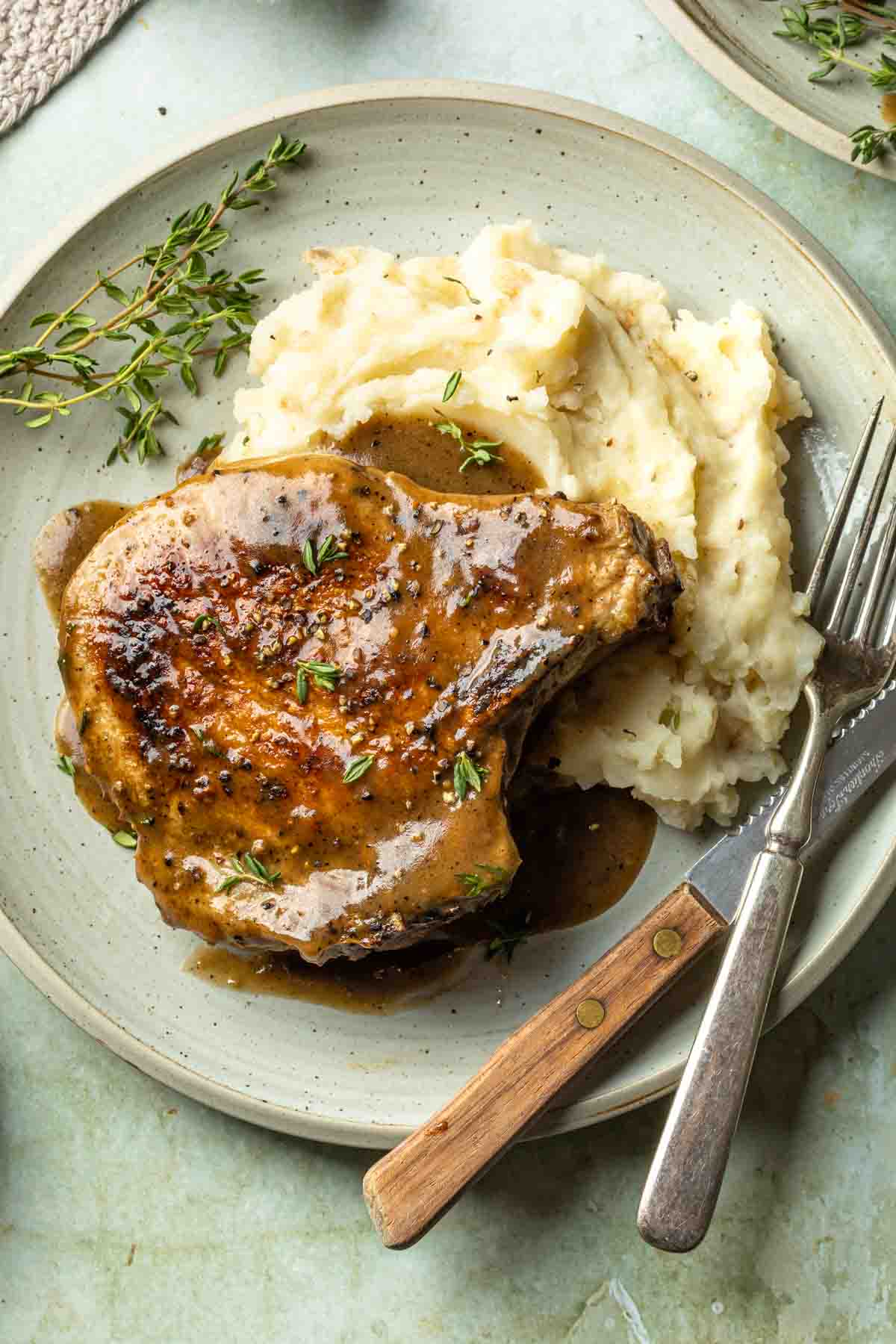 A pork chop with gravy served on a bed of mashed potatoes. 