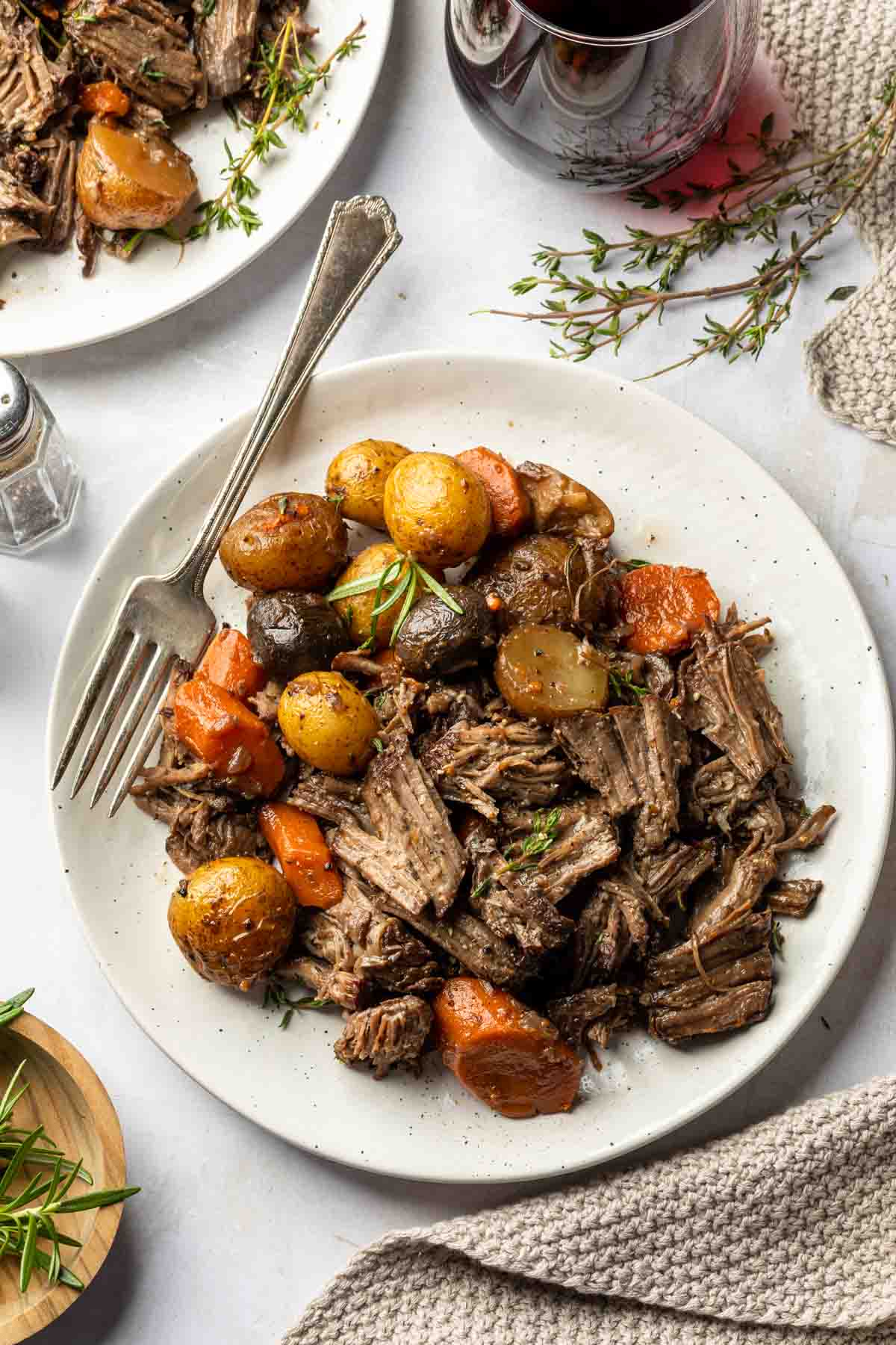 Roast chuck with potatoes and carrots on a plate with rosemary sprigs. 
