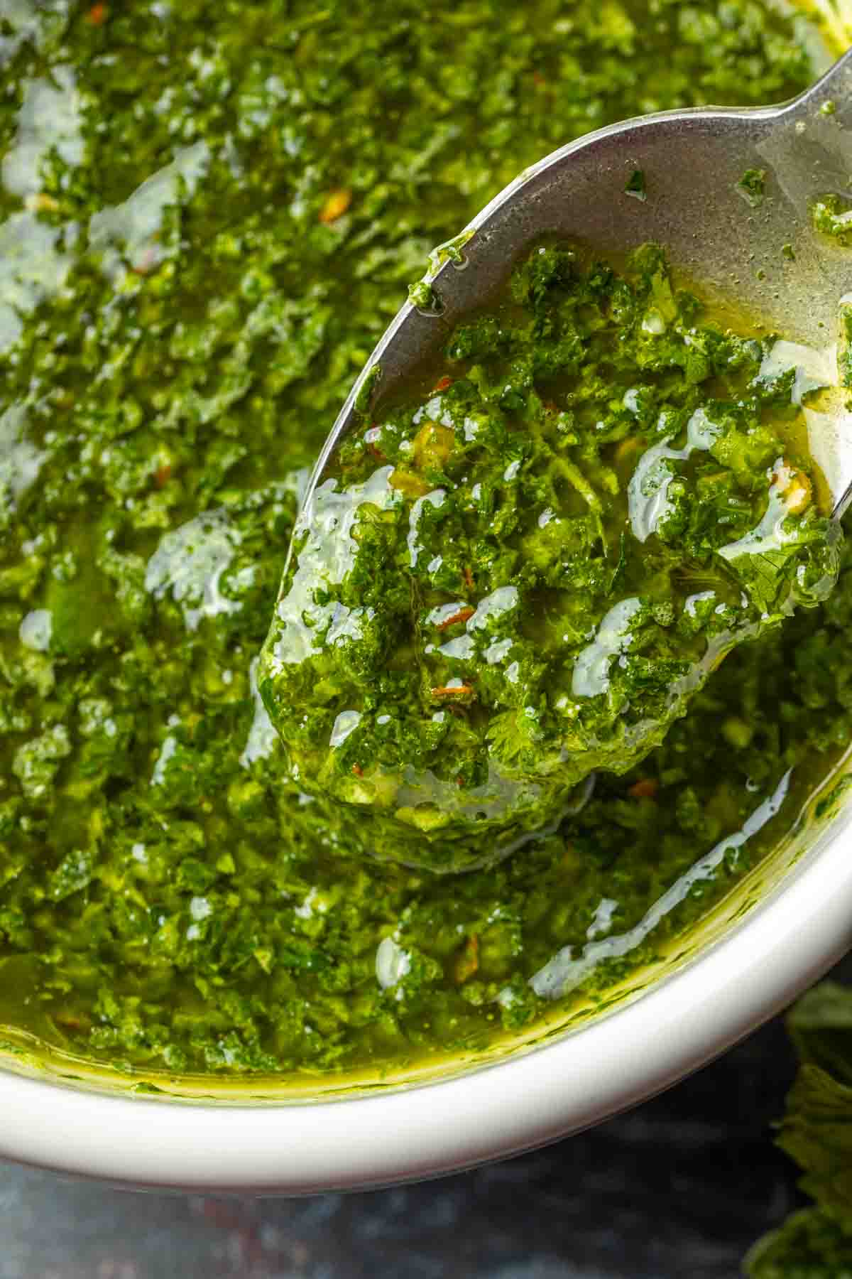 Close up of mint chimichurri sauce in a bowl being spooned. 