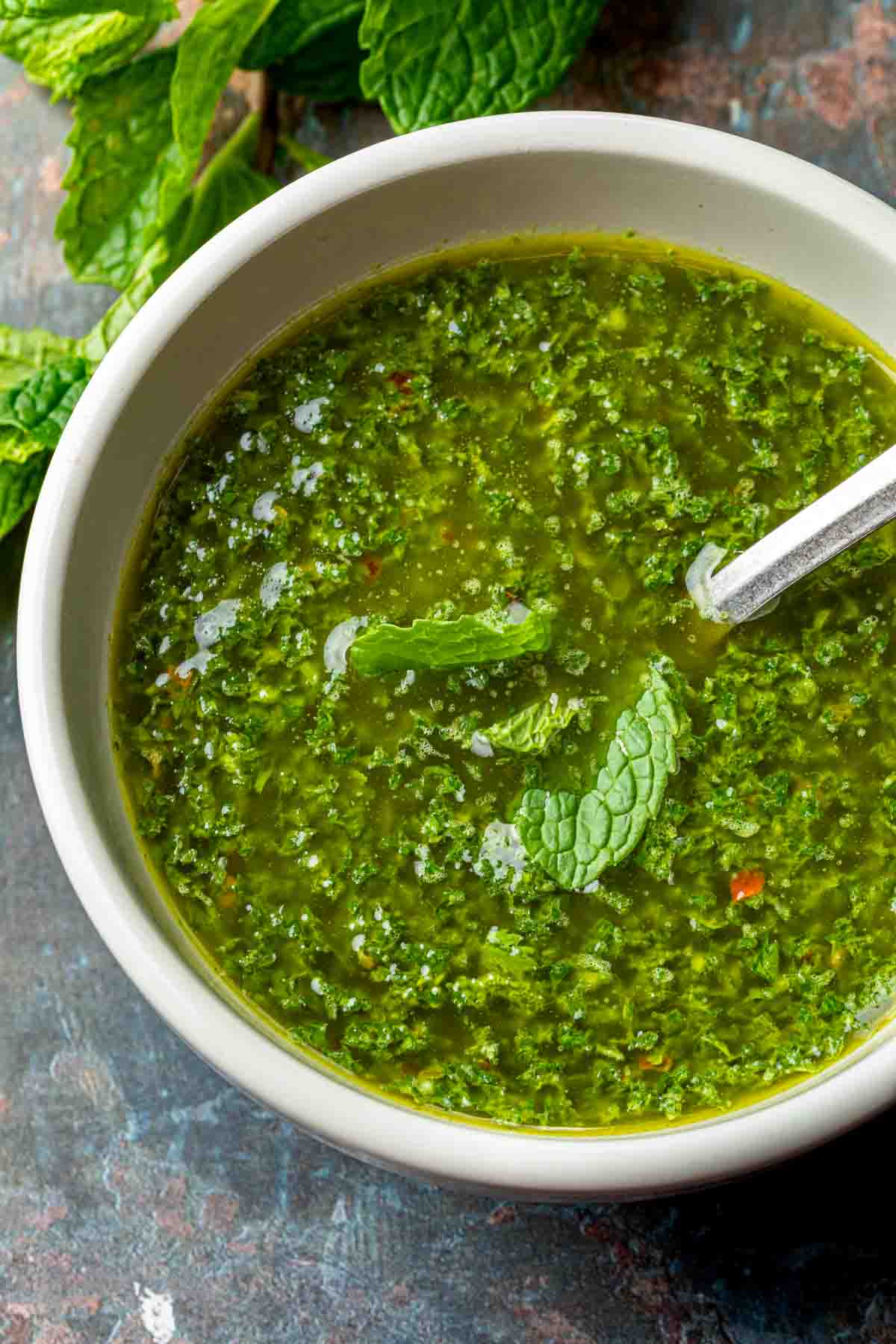 Close up of mint chimichurri sauce in a bowl with a spoon. 