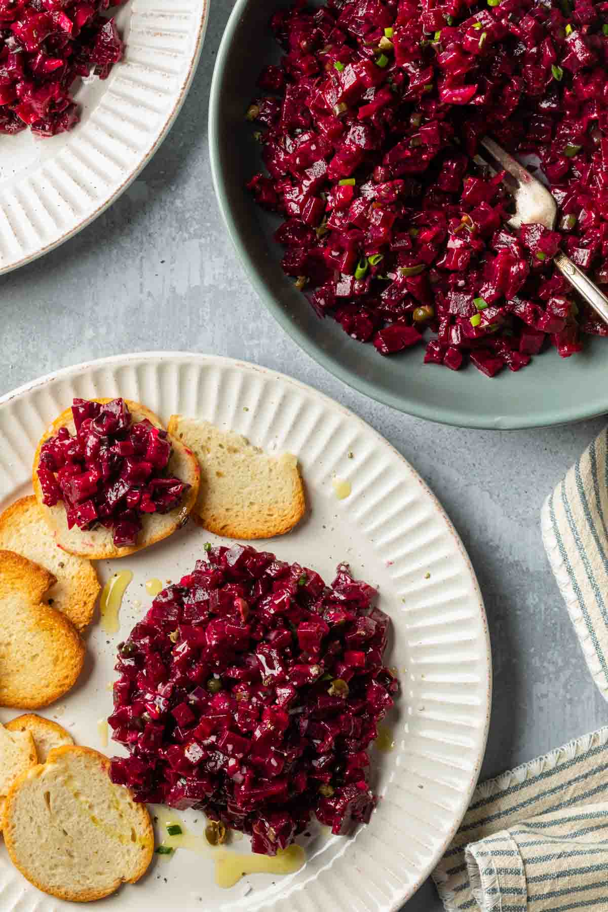 Beetroot tartare in a serving bowl next to a plate with tartare served with crostinis. 