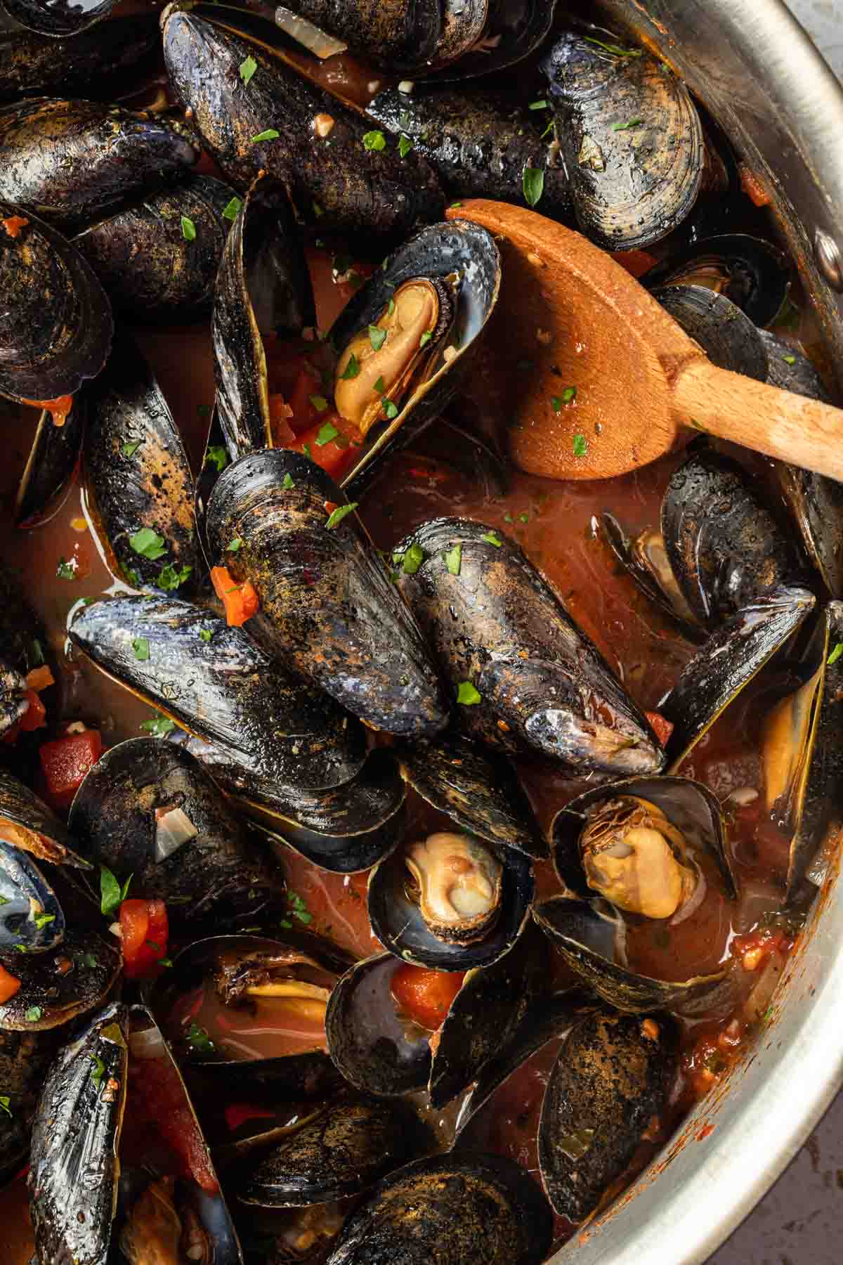 Steamed mussels in a pot with a wooden spoon. 