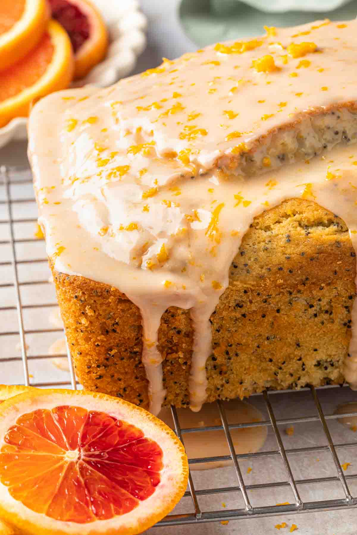 A loaf cake with glaze drizzled over it and down the sides sprinkled with orange zest. 