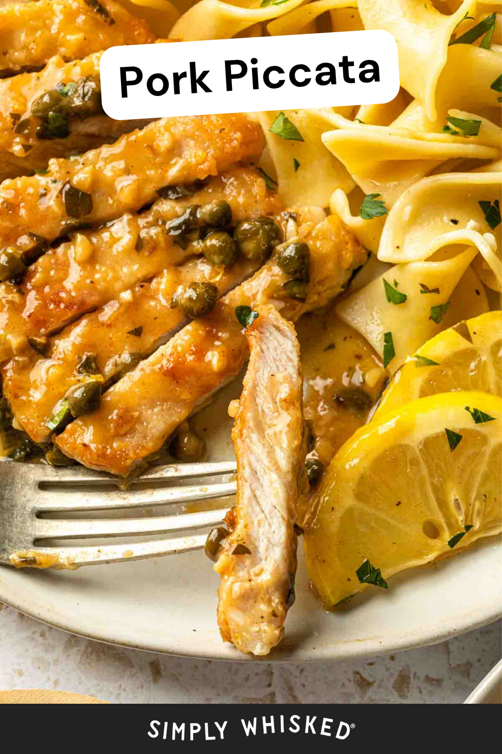 Close-up of pork piccata with capers and sauce, the pork piccata sliced and served with lemon wedges and egg noodles, garnished with parsley. A fork is beside the food on a white plate.