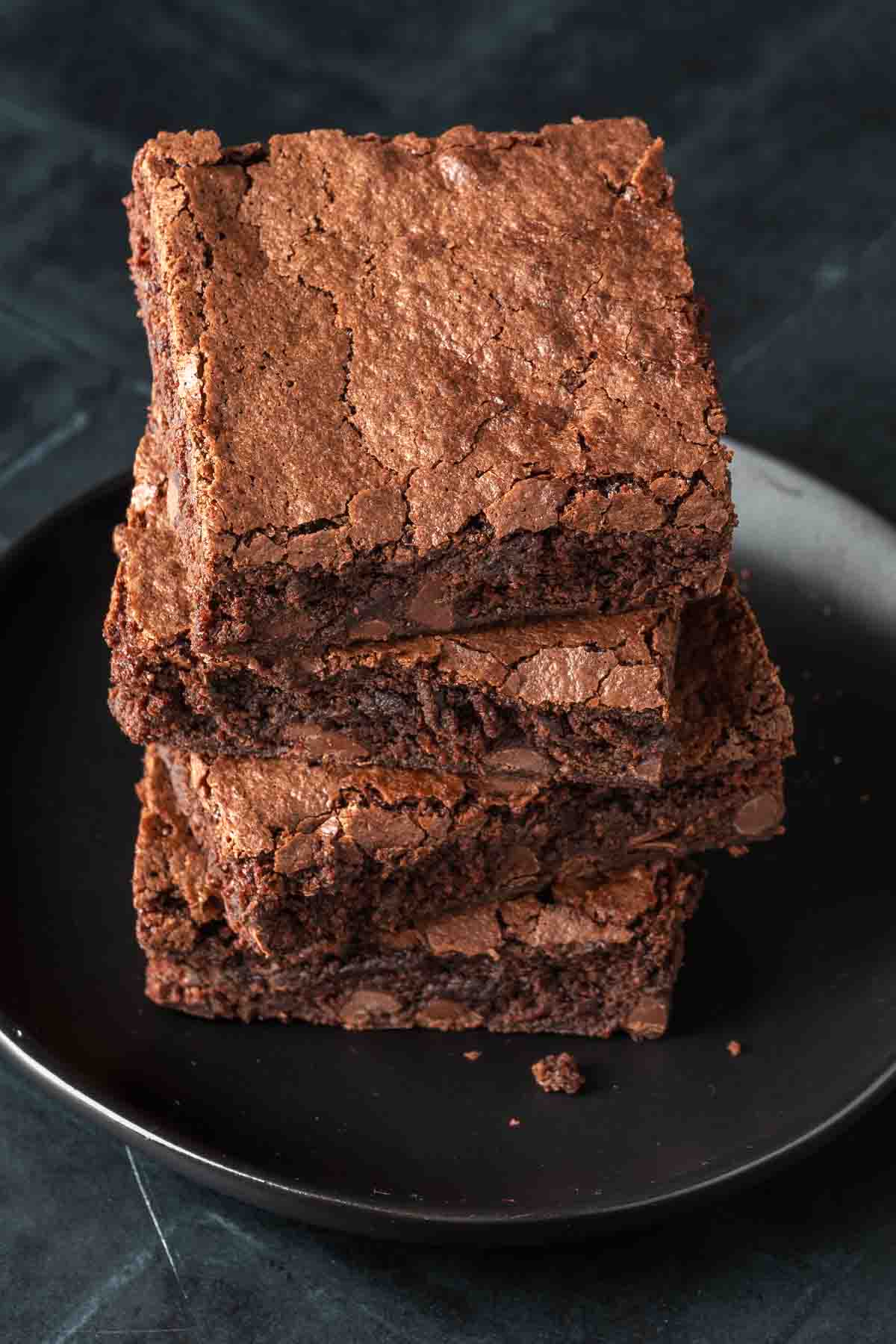 A stack of 3 brownies on a black plate. 