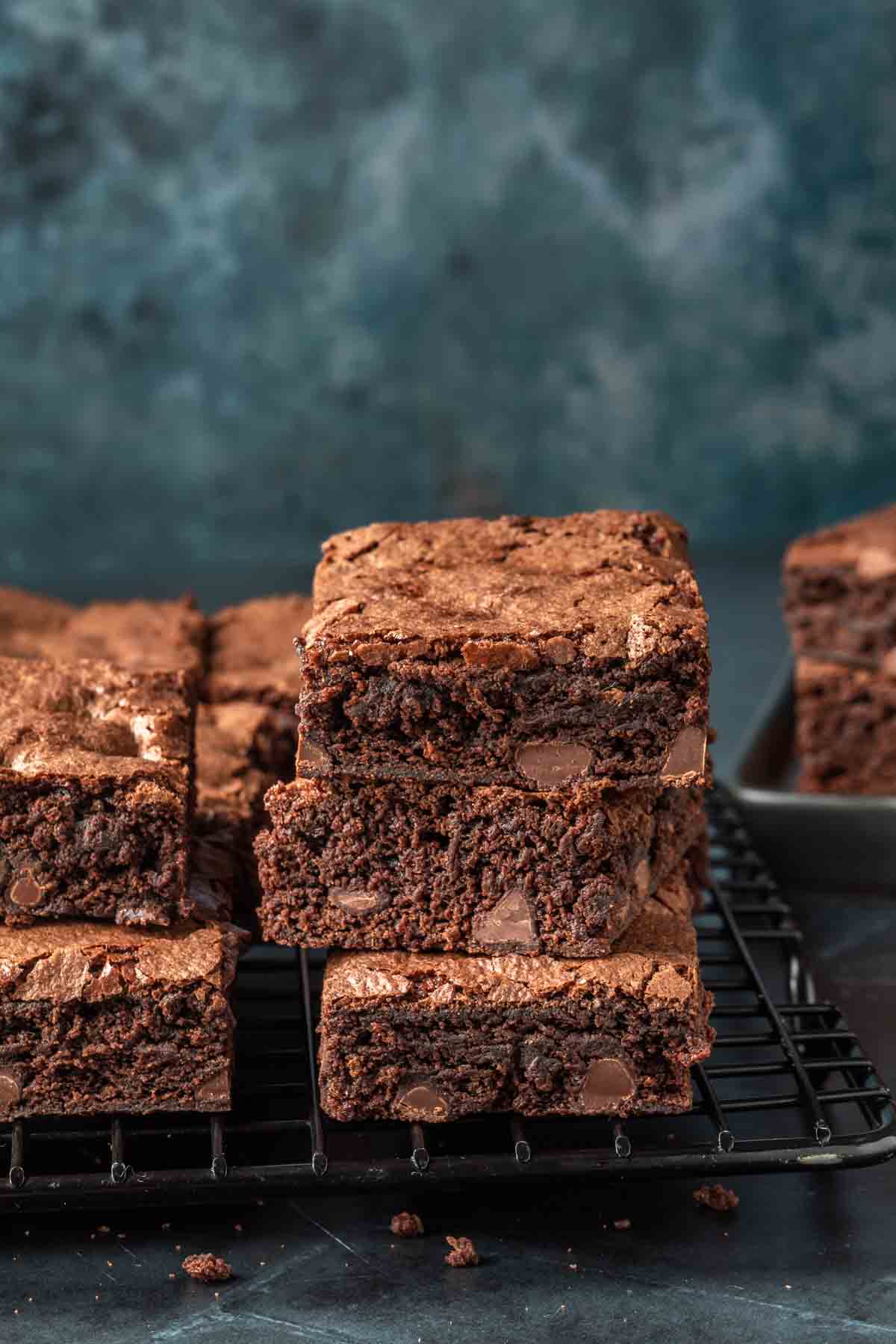 A stack of brownies, with the rest of the brownies surrounding on a cooling rack. 