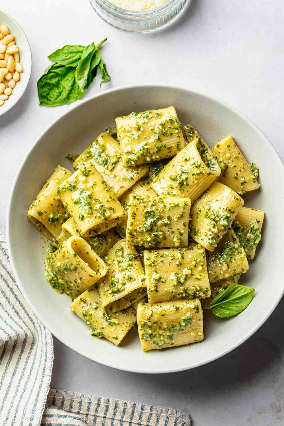 Rigatoni with dairy free pesto sauce in a bowl garnished with a fresh basil leaf. 
