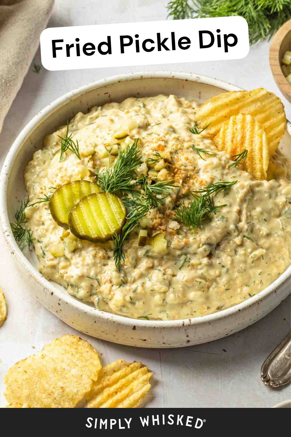 A bowl of creamy fried pickle dip garnished with dill and pickle slices, served alongside ridged potato chips. The text Fried Pickle Dip appears at the top, with Simply Whisked at the bottom for a delicious presentation.