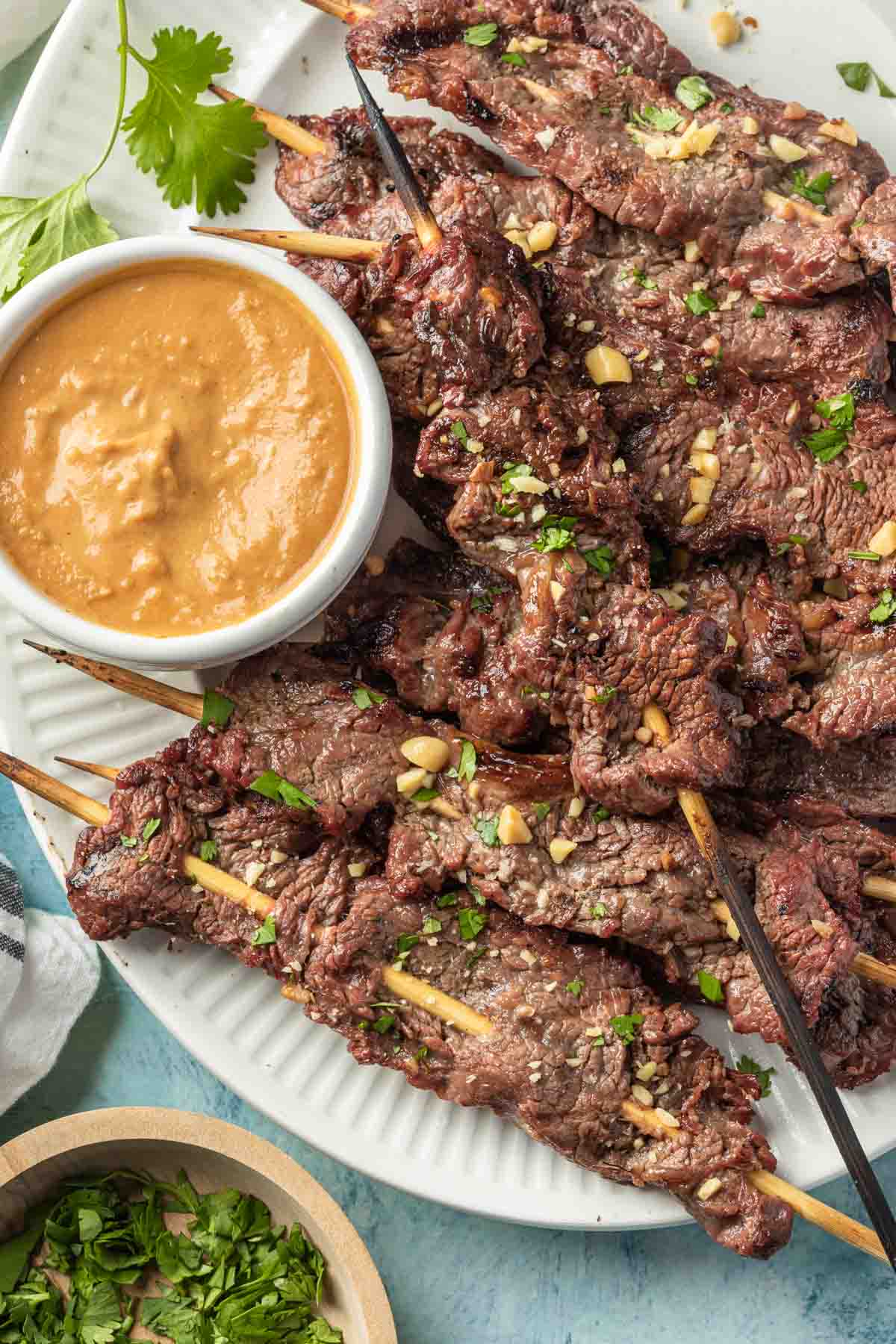 Beef satay skewers on a platter garnished with fresh chopped cilantro and peanuts. 