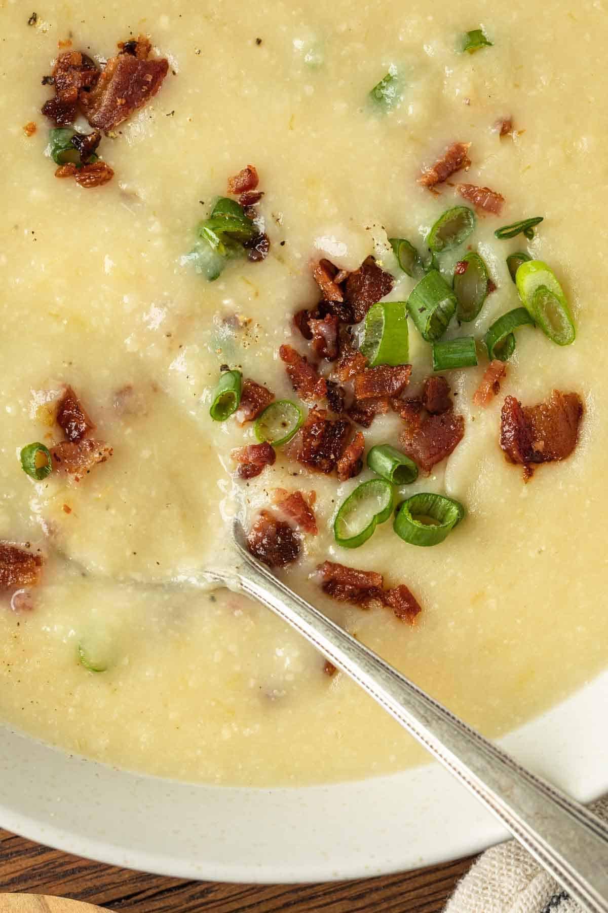 Close up of bacon bits and green onions in a creamy potato soup. 