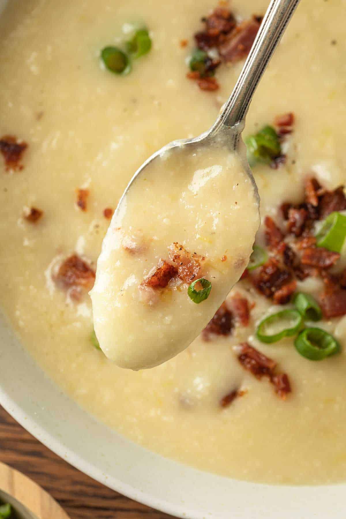 Creamy potato soup on a spoon with a bowl of the soup in the background. 