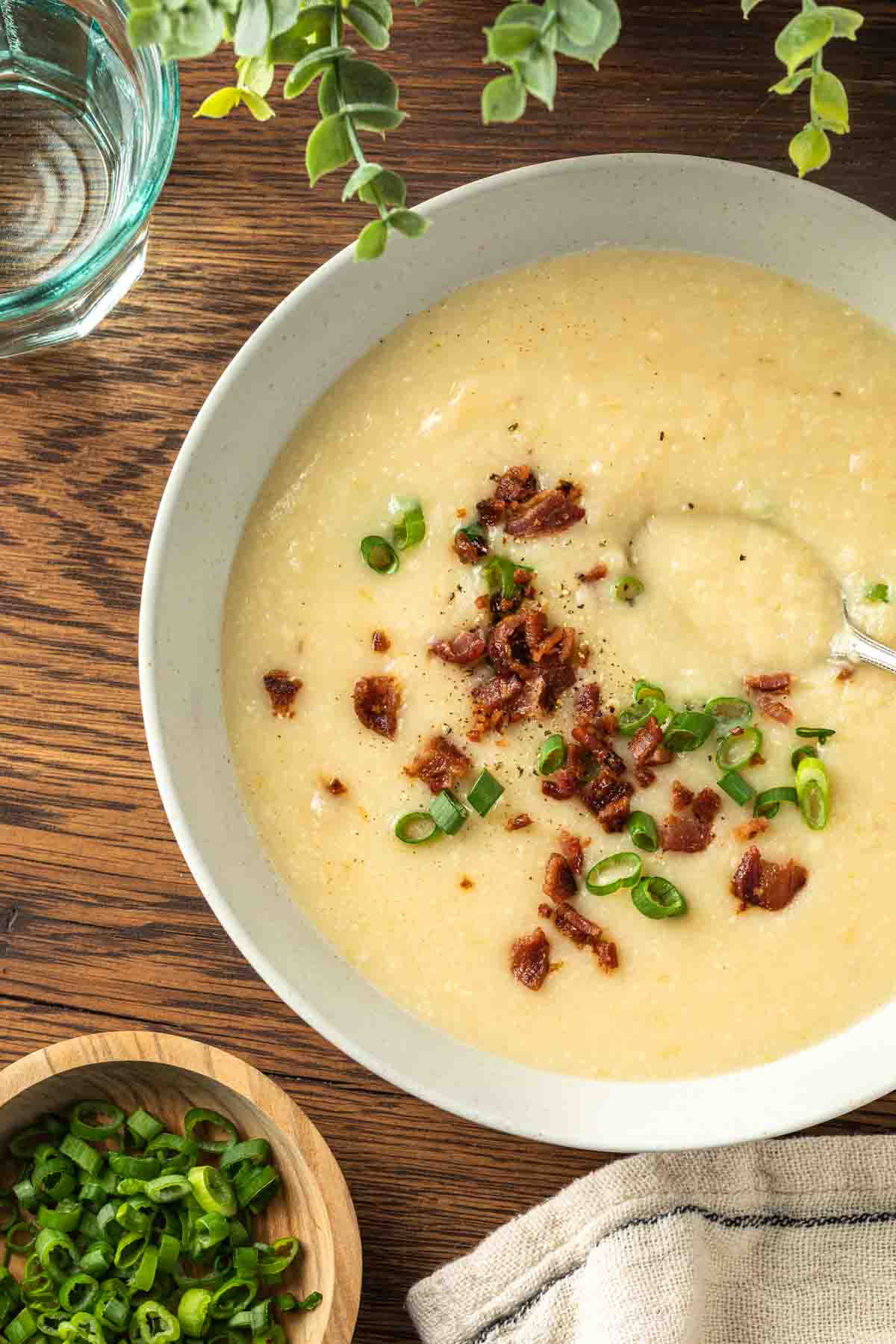 A bowl of cauliflower potato soup with bacon and green onions garnishing the bowl. 