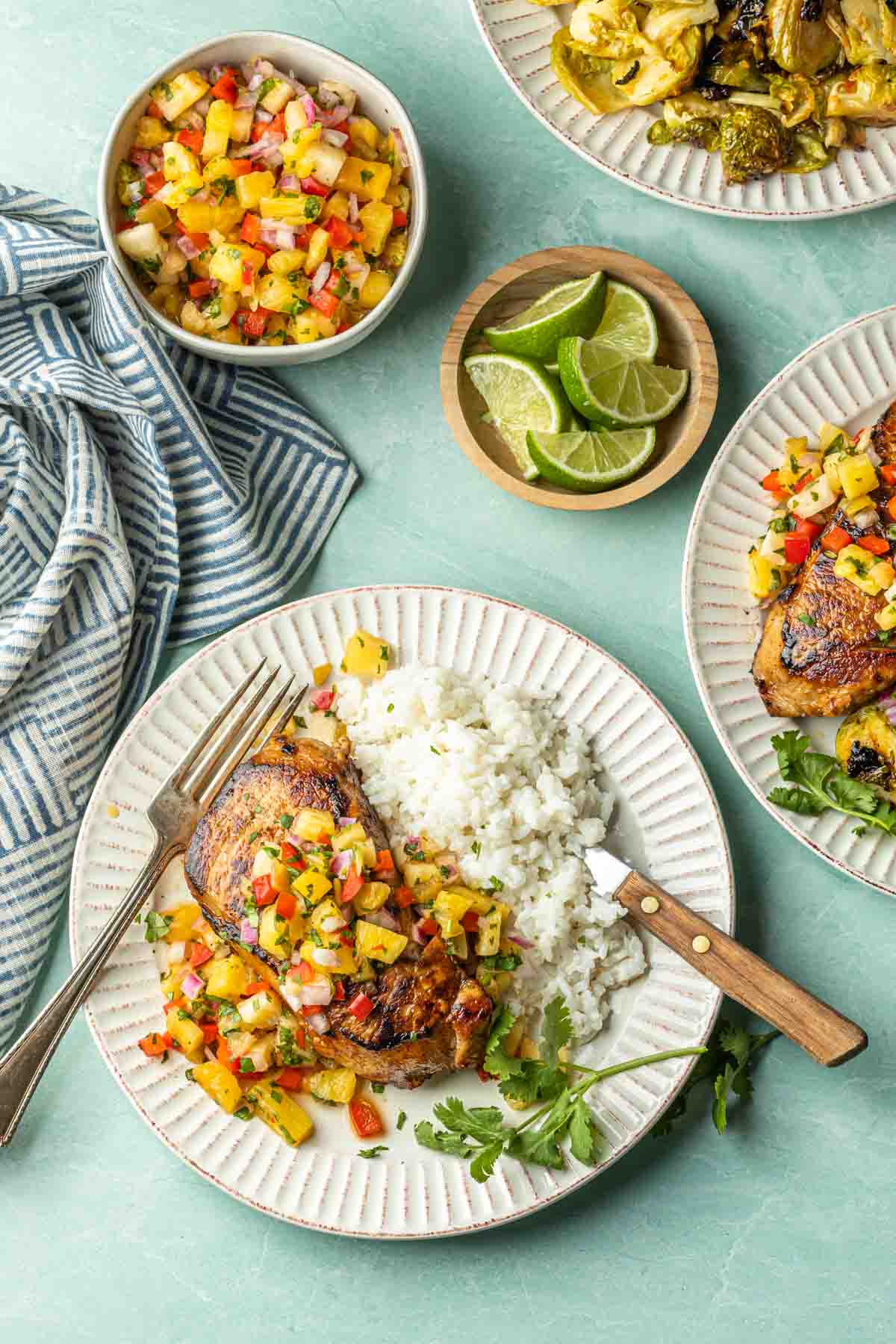 An overhead shot of a few plates with  seared pork chops topped with pineapple salsa served next to a bed of coconut rice. 