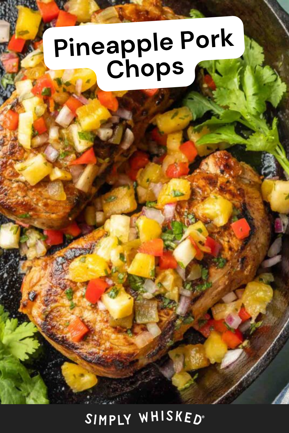 Two cooked Pineapple Pork Chops topped with a colorful pineapple salsa, garnished with fresh cilantro, served in a skillet. The text Pineapple Pork Chops appears at the top, and Simply Whisked at the bottom.