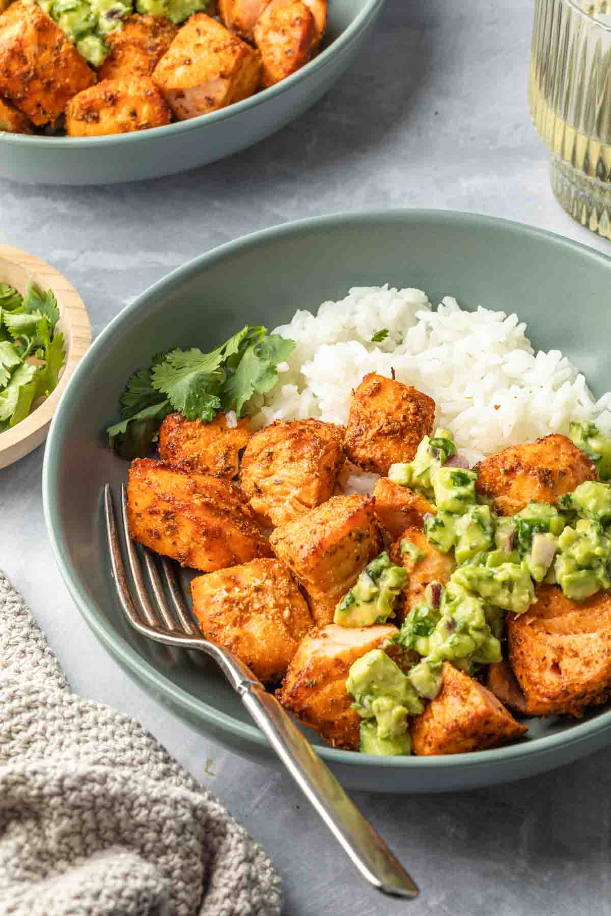 Salmon pieces in a bowl with jasmine rice and a fresh green salsa. 
