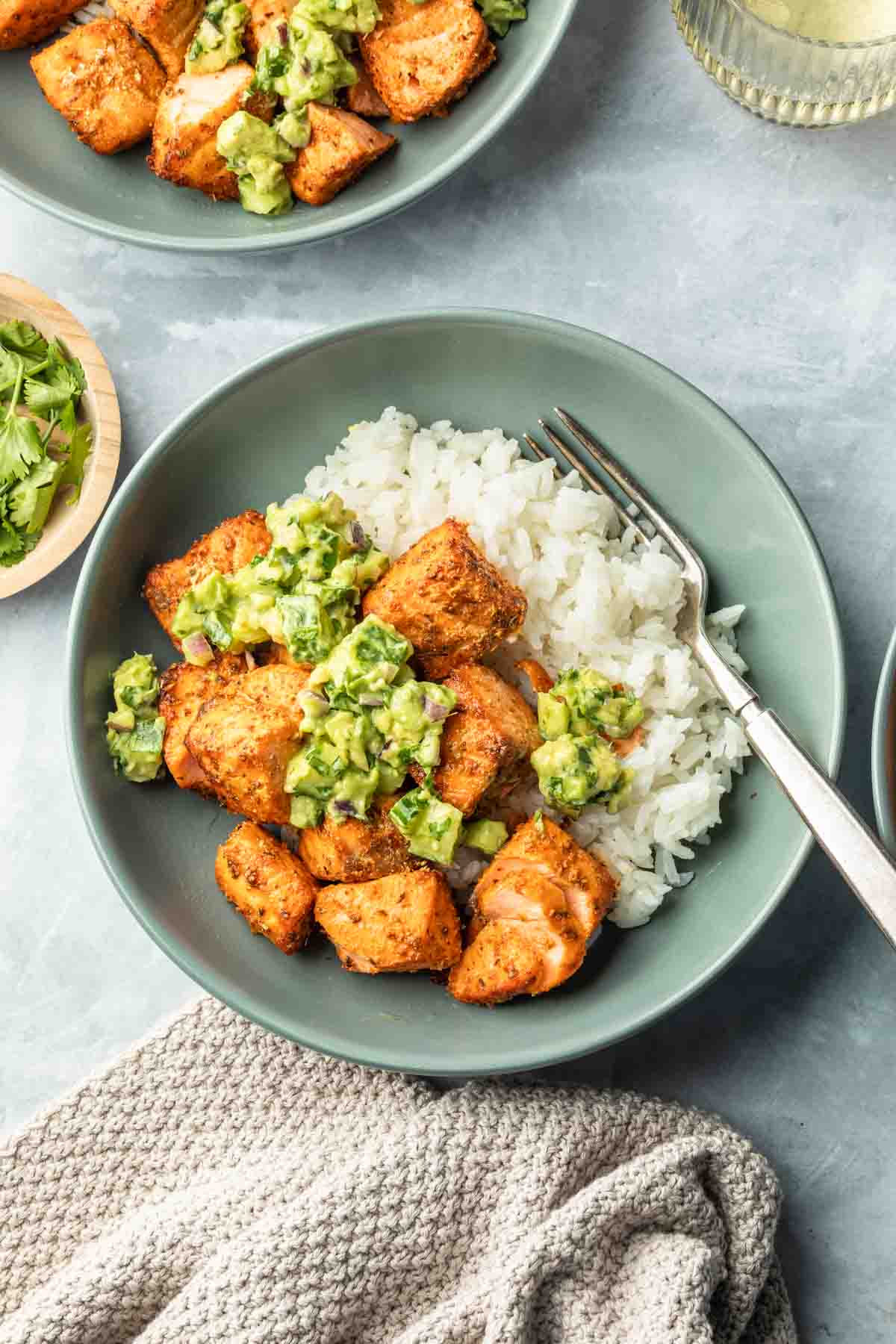 A bowl of blackened air fryer salmon bites topped with avocado cucumber salsa over a bed of rice. 