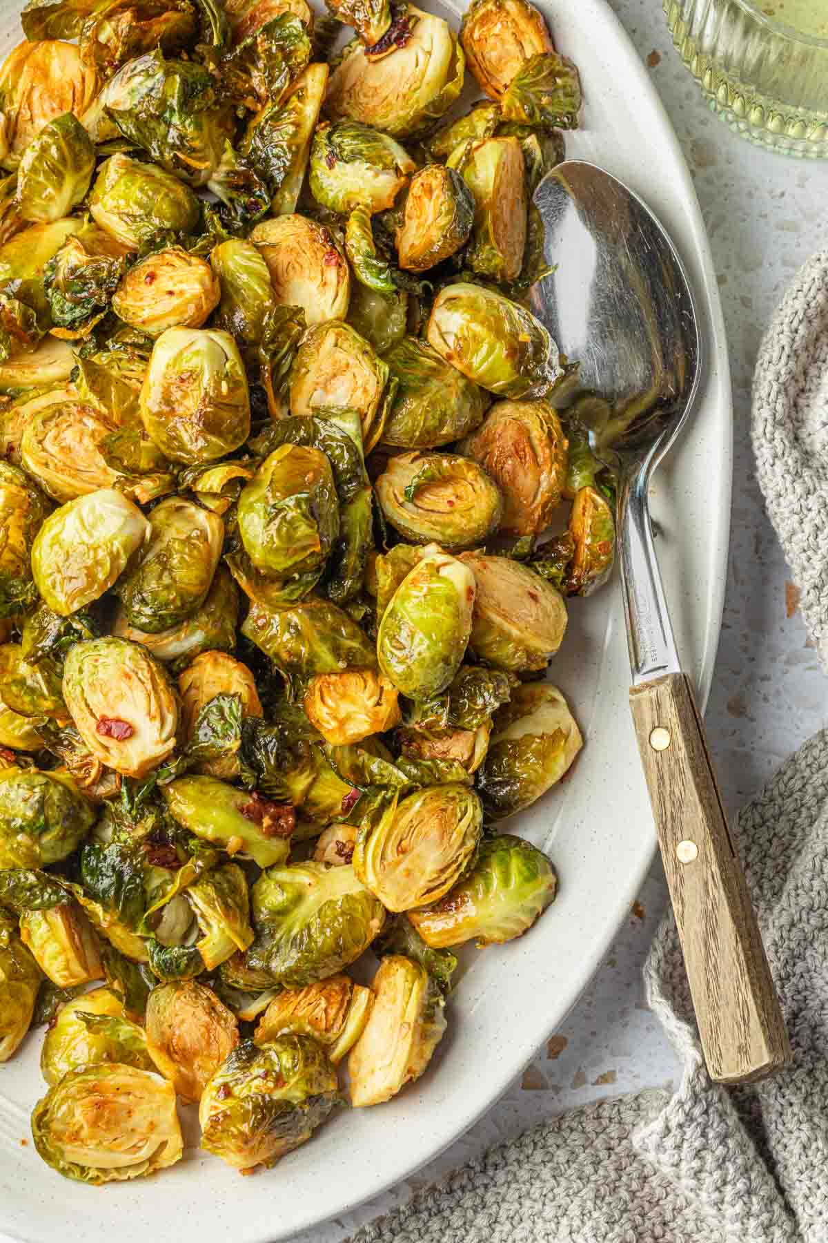 A serving platter of chipotle maple smoked brussels sprouts with a spoon resting in it. 