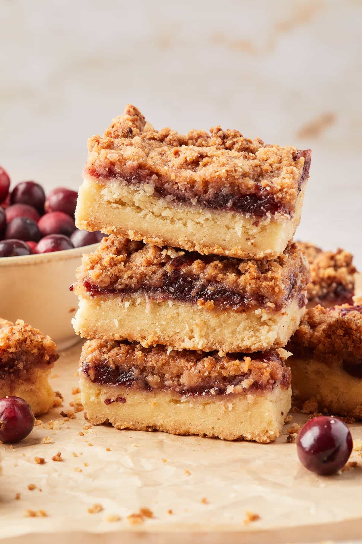 A stack of fruit preserves shortbread bars with a bowl of cranberries in the background. 