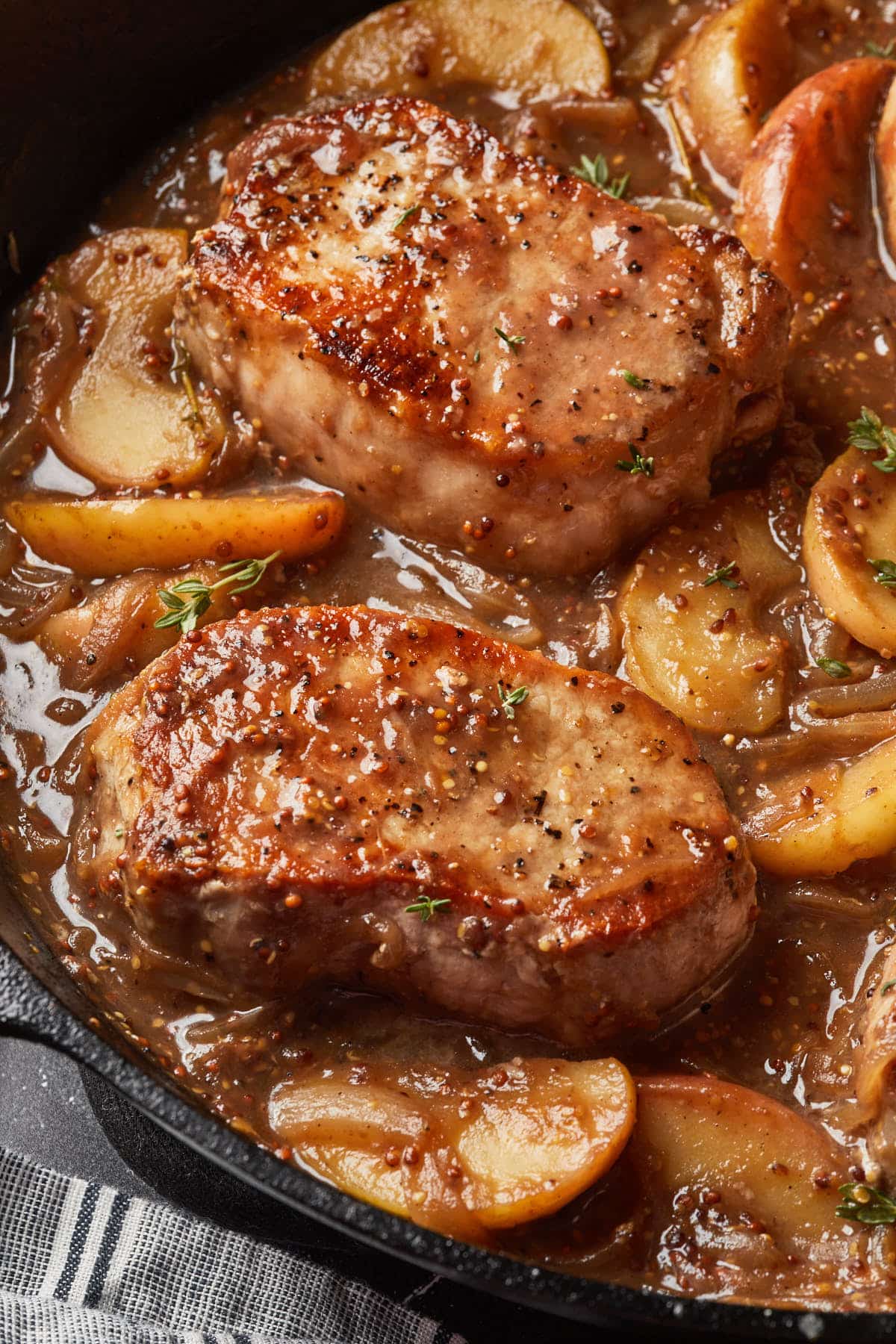 Close up of pork chops in a cast iron skillet with apples and fresh thyme in a sweet and savory gravy. 