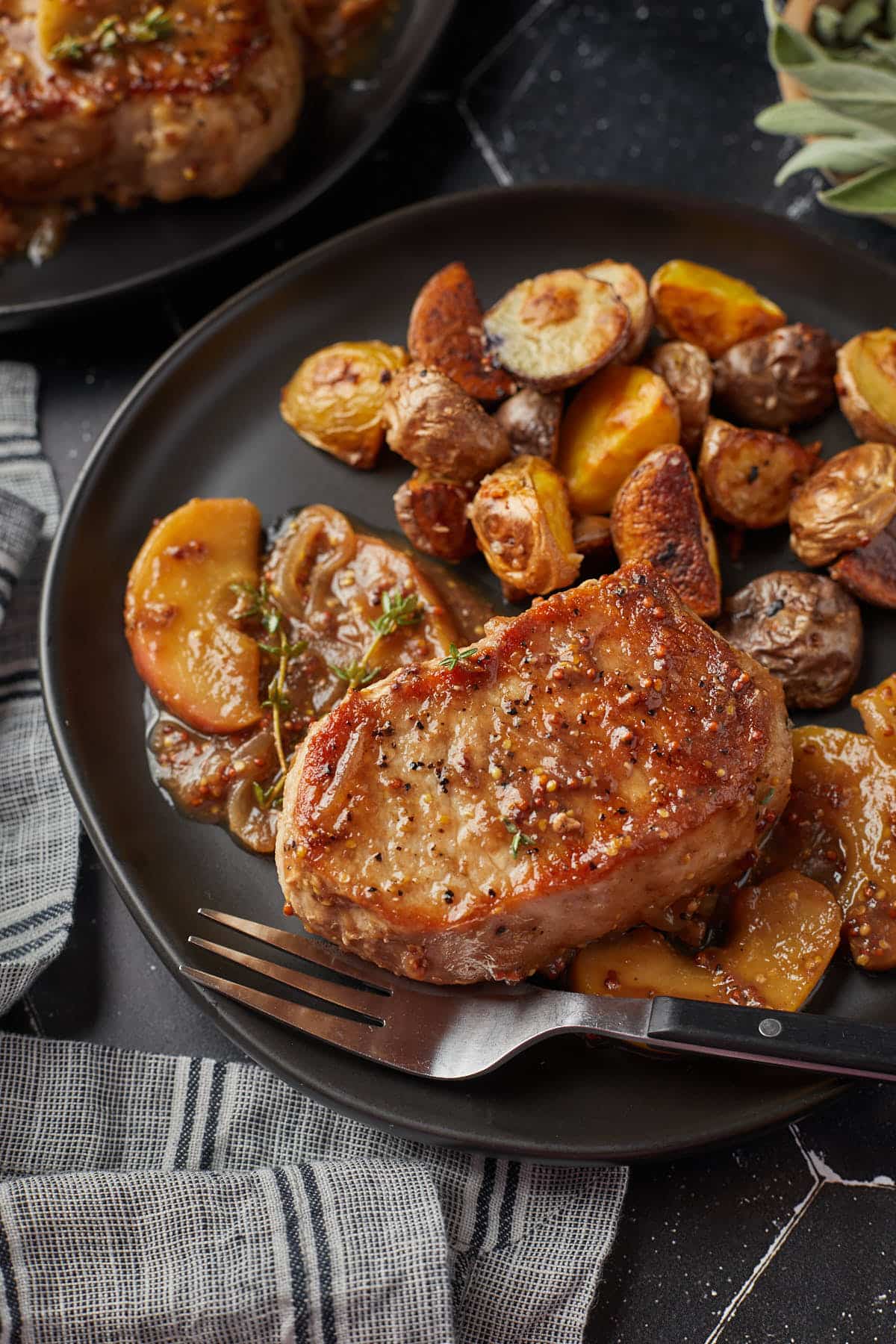 A plate of apple butter pork chops served with roasted potatoes and garnished with fresh thyme. 