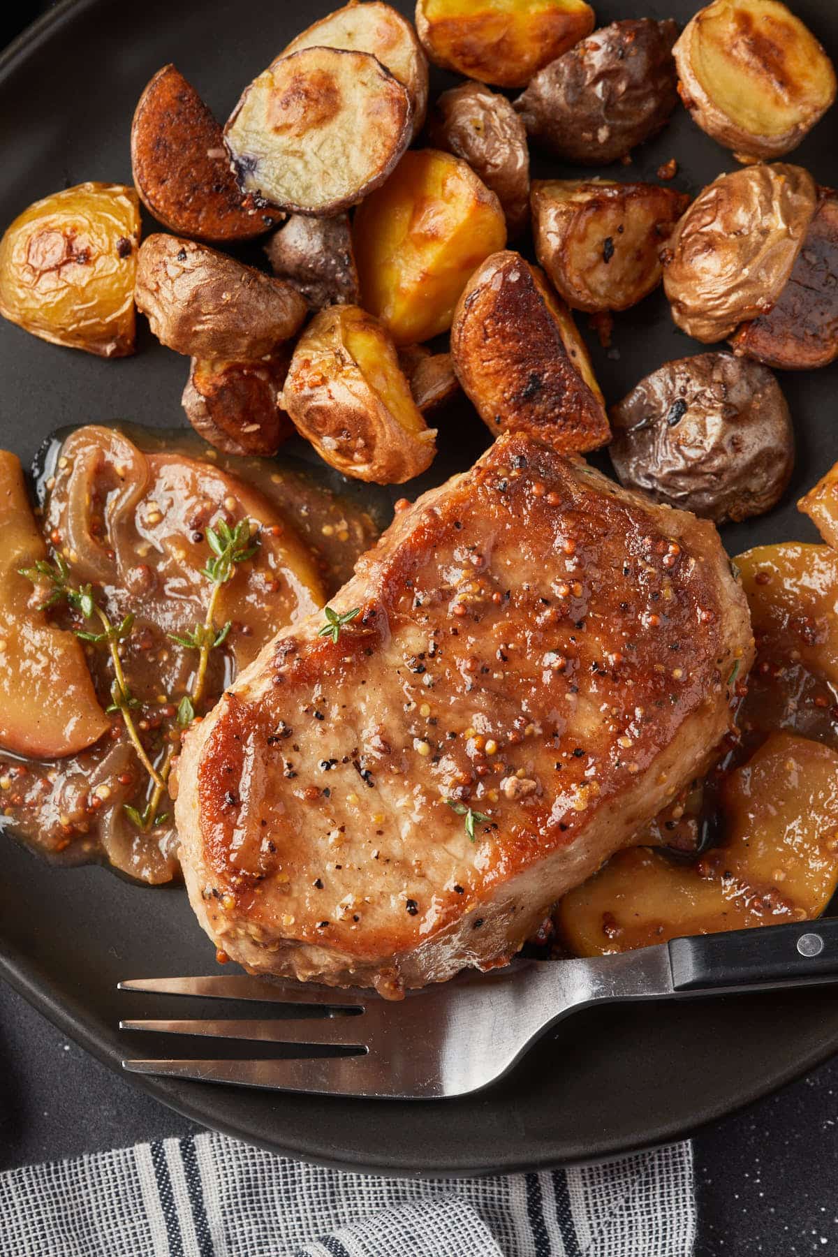 A serving of  a sweet and savory pork on a plate with roasted potatoes. 