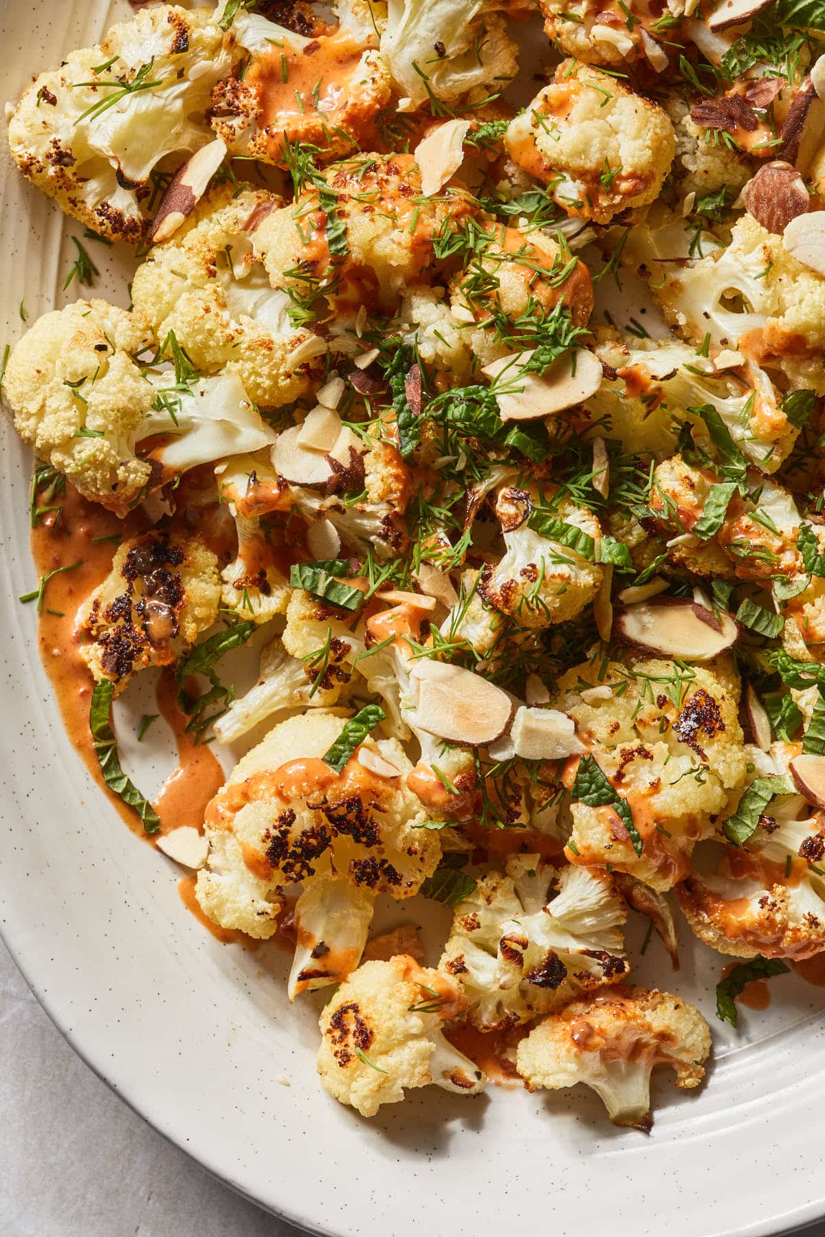 Close up of roasted cauliflower with a drizzle of tahini harissa sauce. 