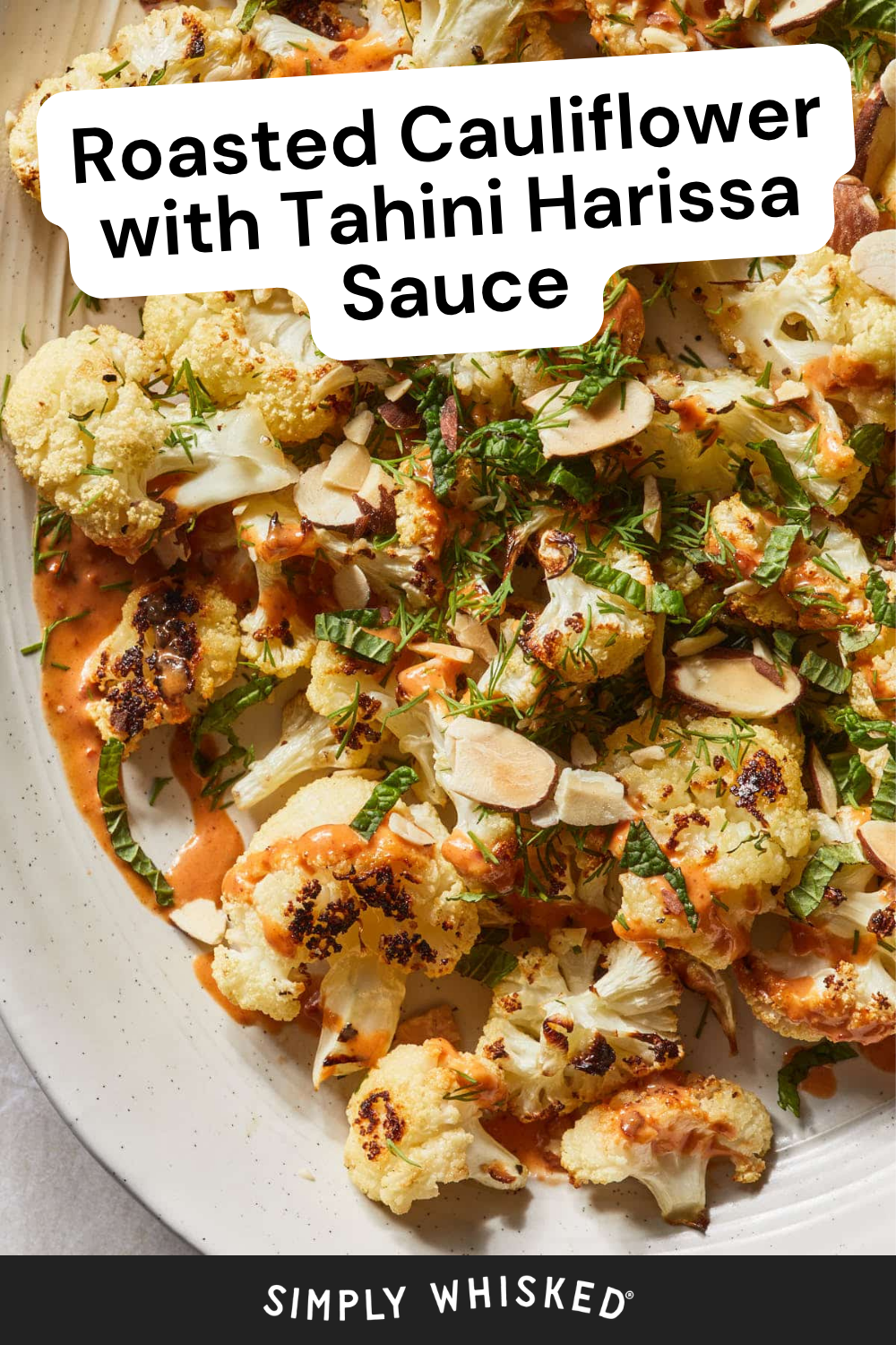Close-up of Harissa Roasted Cauliflower topped with sliced almonds, fresh herbs, and creamy orange tahini harissa sauce on a white platter. Text reads: Roasted Cauliflower with Tahini Harissa Sauce.