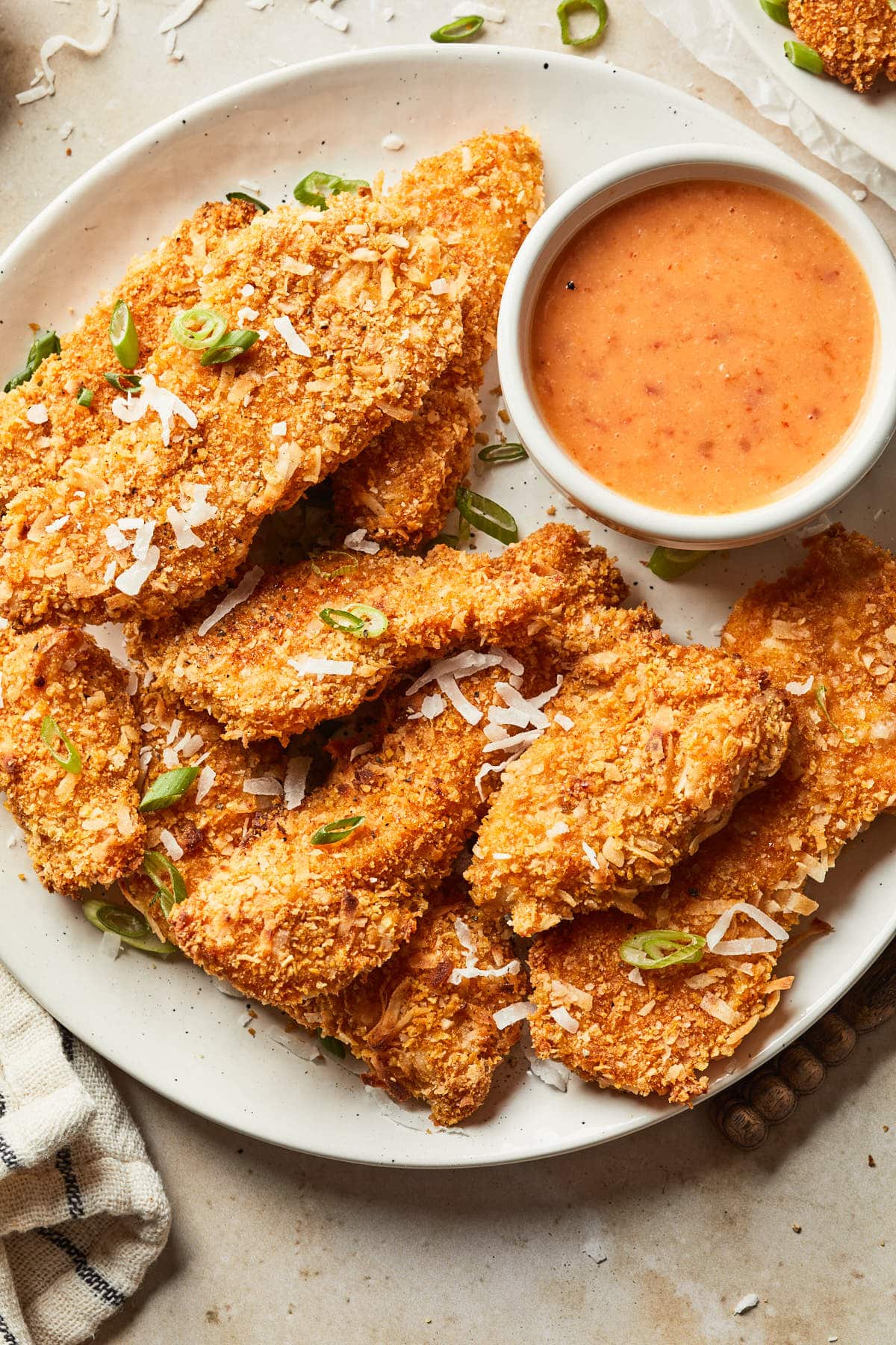 Close up of coconut chicken tenders garnished with coconut flakes and green onions.