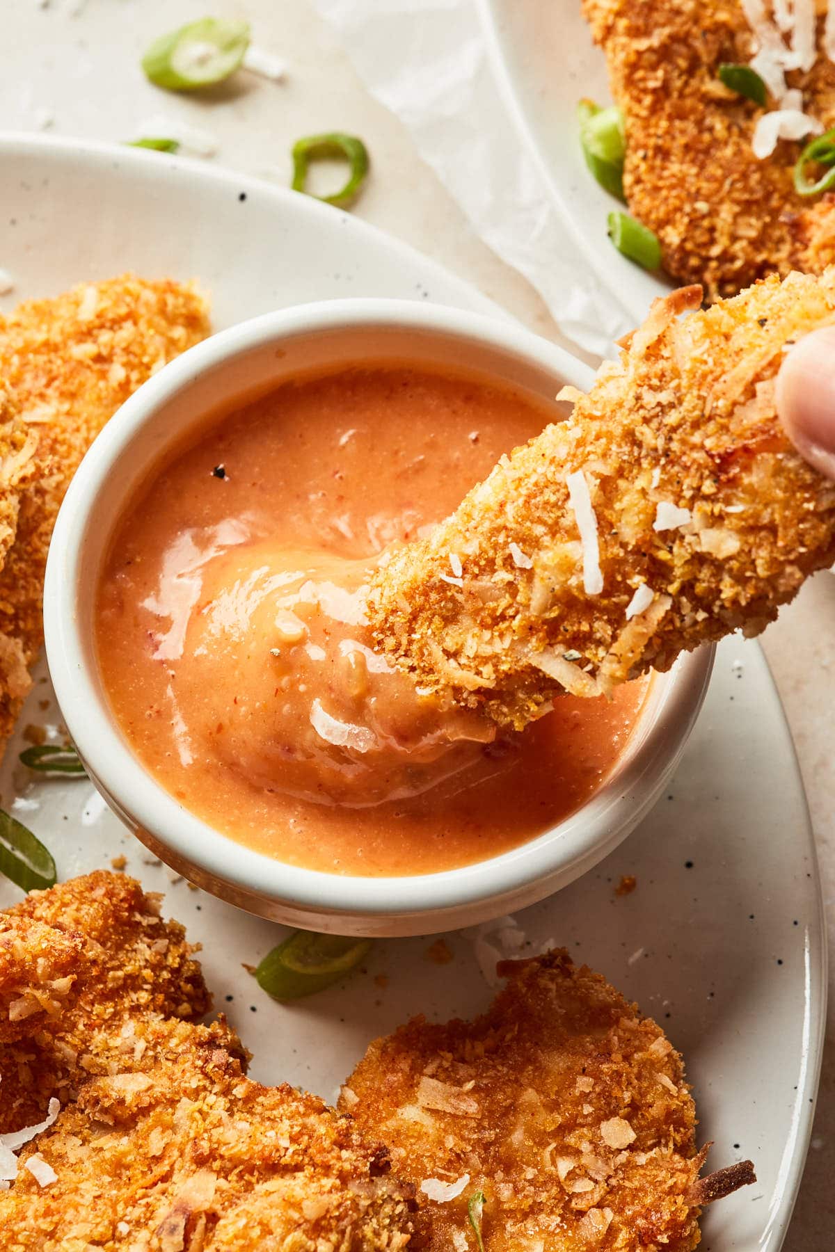A piece of chicken being dipped into a sauce.