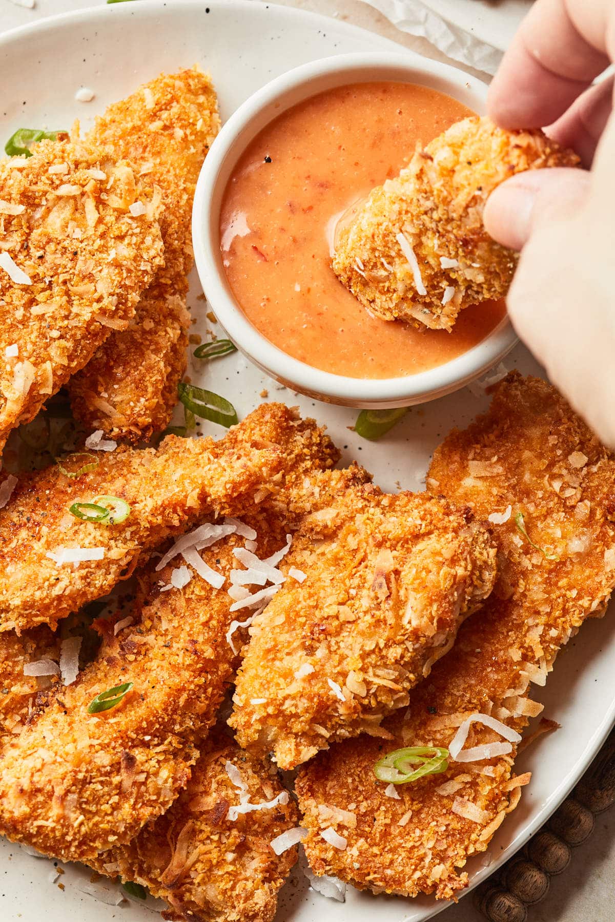 A hand dipping a piece of chicken into a dipping sauce.