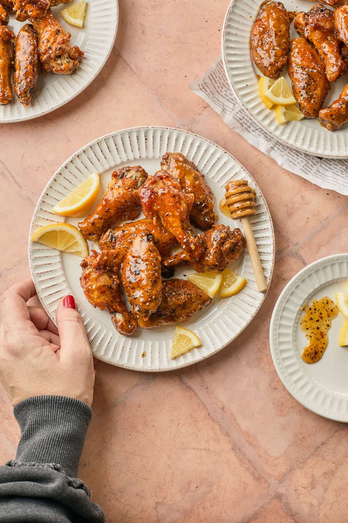 A plate of hot honey lemon pepper wings being served with lemon wedges.