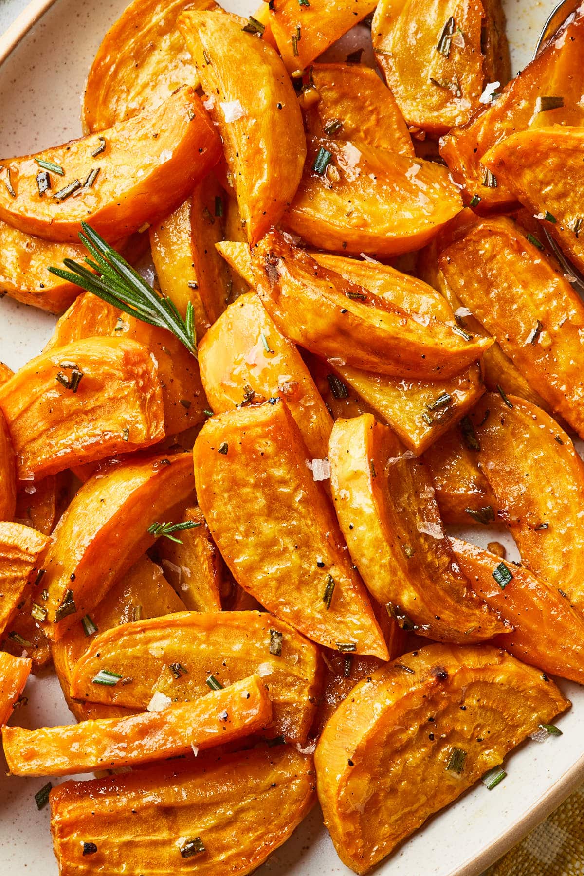 Close up of roasted golden beets on a serving platter with a sprig of fresh rosemary.