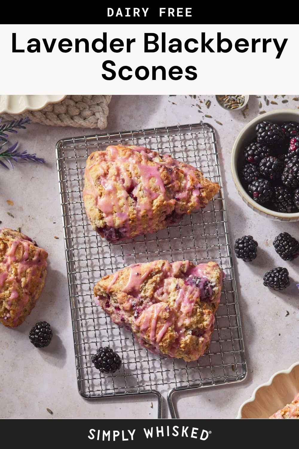 Two triangular Blackberry Scones with pink glaze rest on a cooling rack, surrounded by fresh blackberries and a bowl of berries, with a label reading “Dairy Free Lavender Blackberry Scones” at the top.